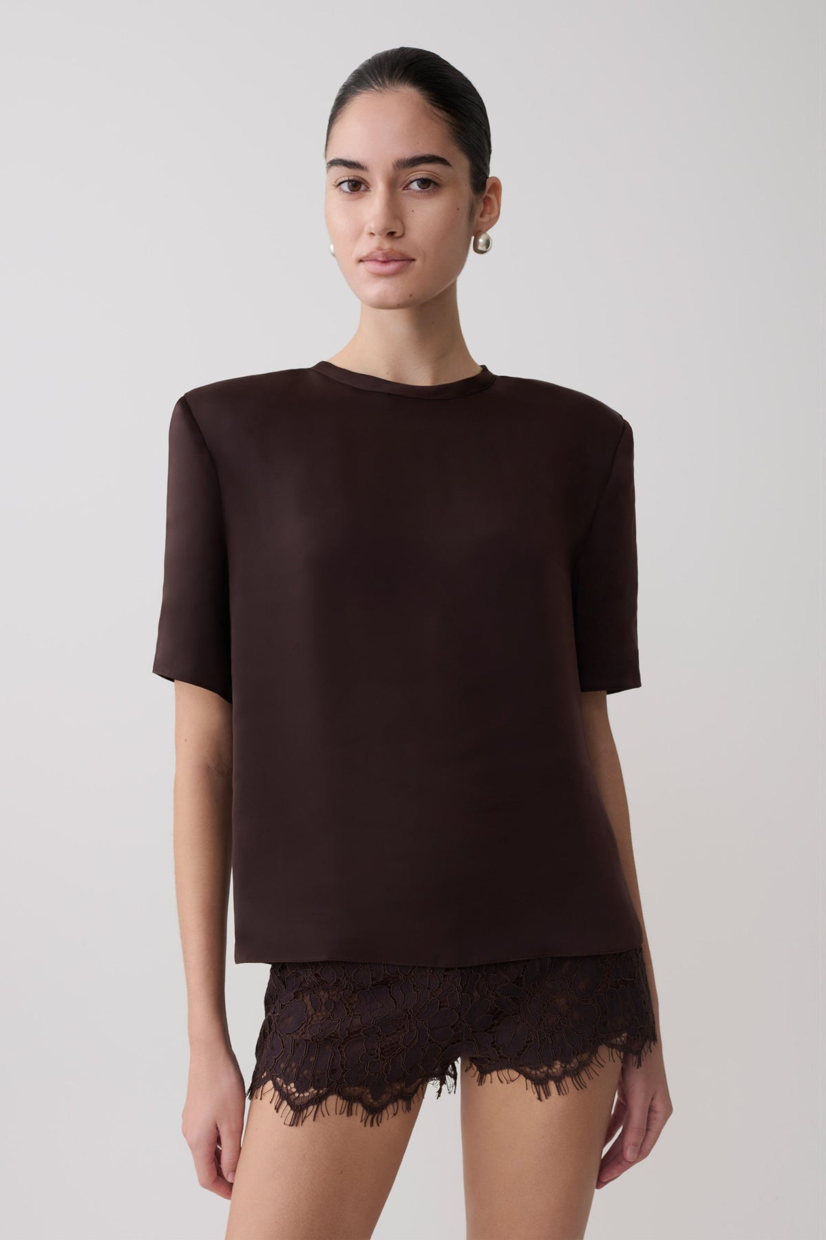 Woman wearing a dark brown shoulder pad short sleeve satin top with matching lace shorts.