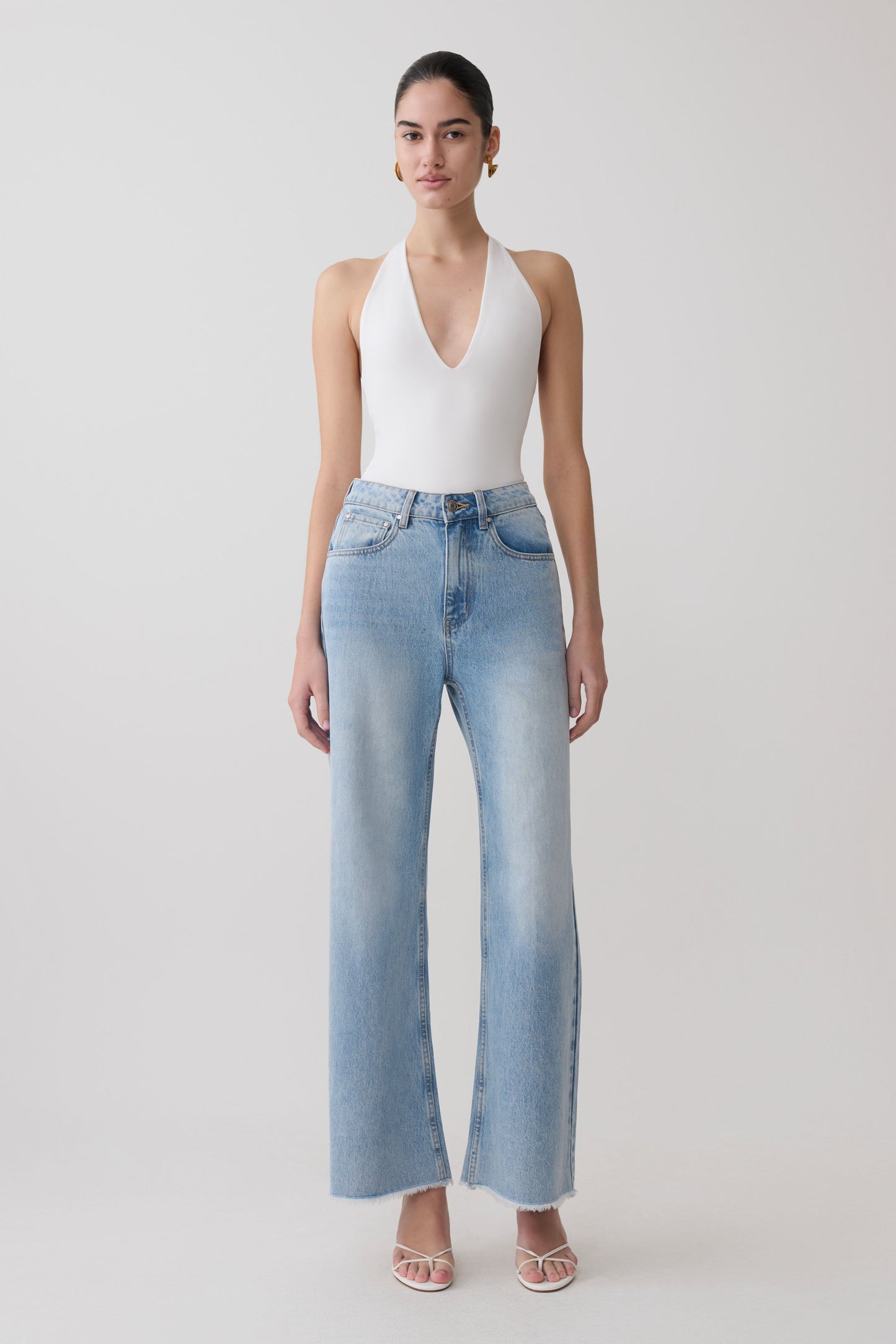 Woman wearing a white slinky halter bodysuit with blue jeans.