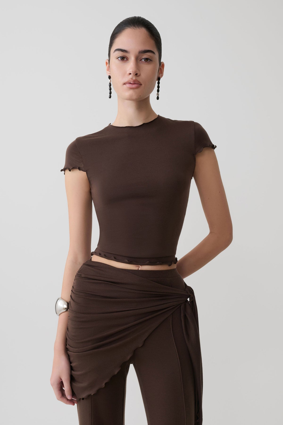 Woman wearing a brown high neck top with piping detail.