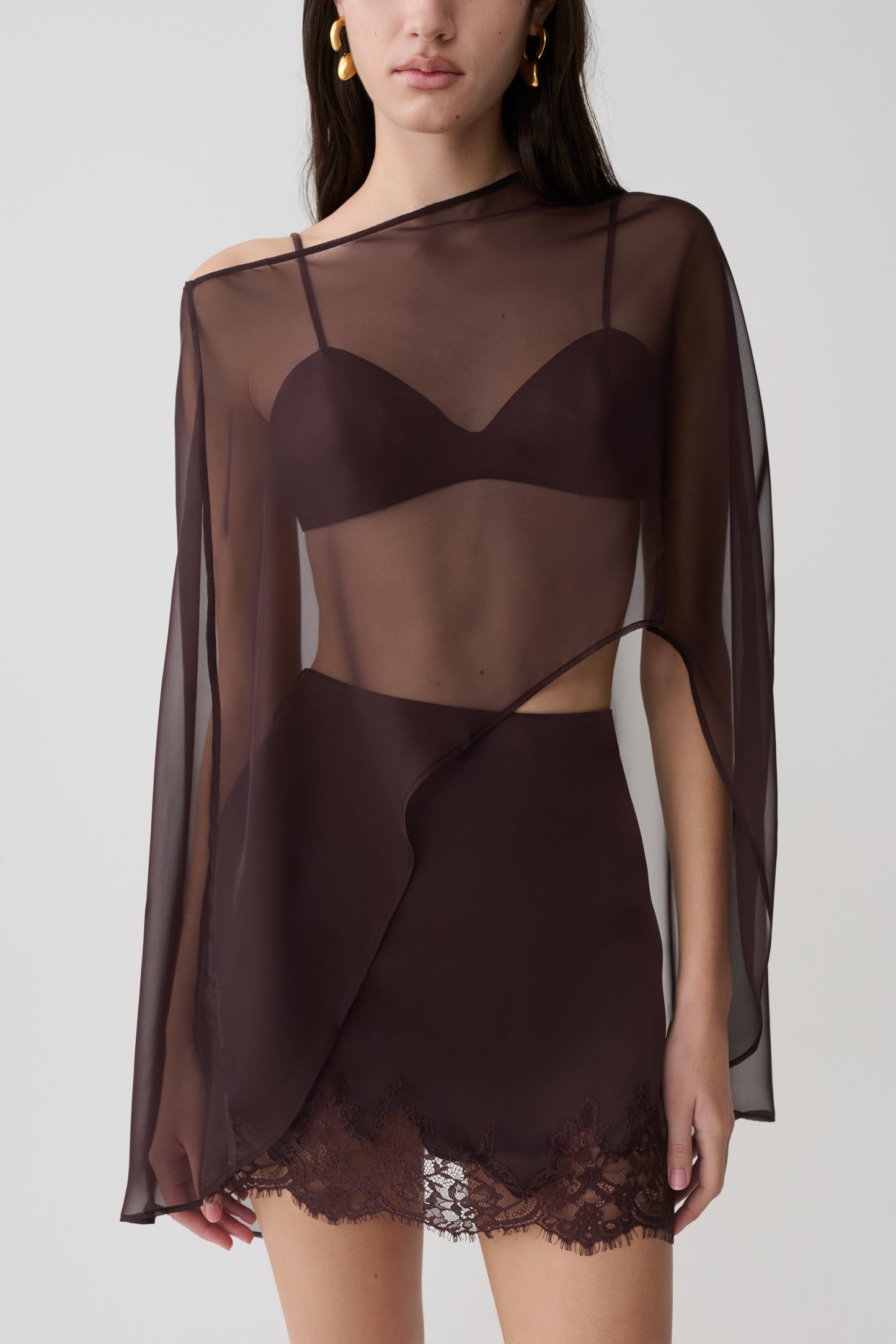 Woman wearing brown bralette with chiffon cape with matching lace and satin mini skirt.