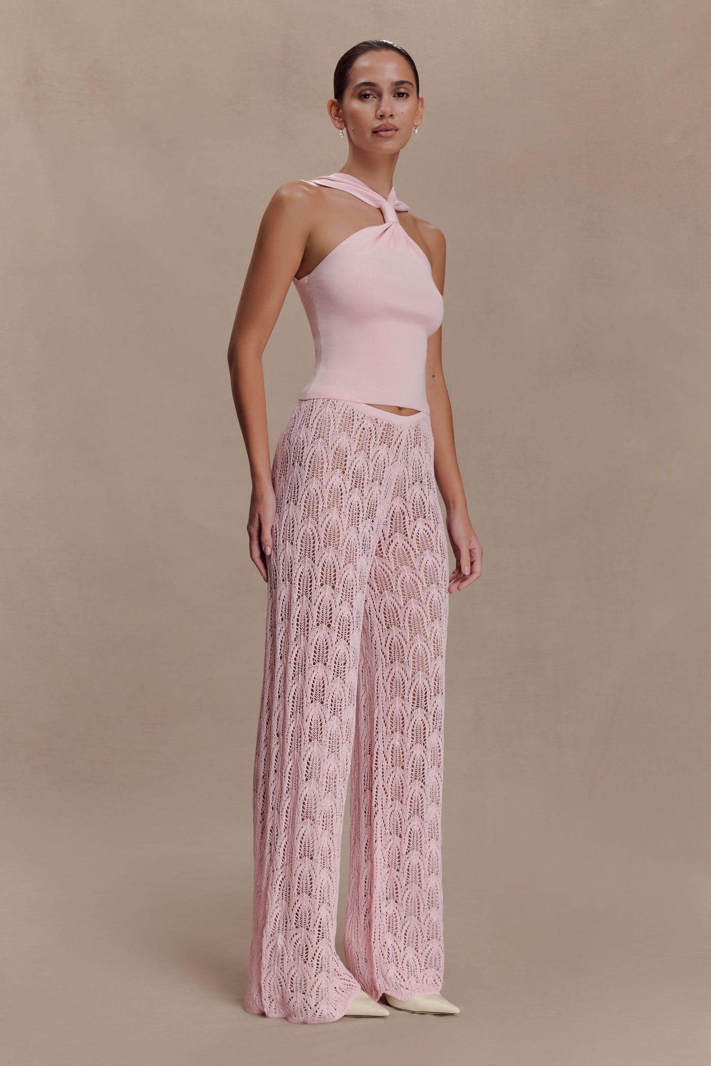 Woman wearing a pink knit top and crochet pants.