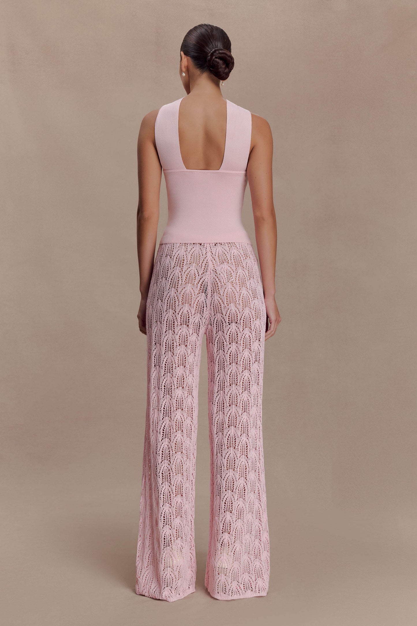 Woman wearing a pink knit top and crochet pants.