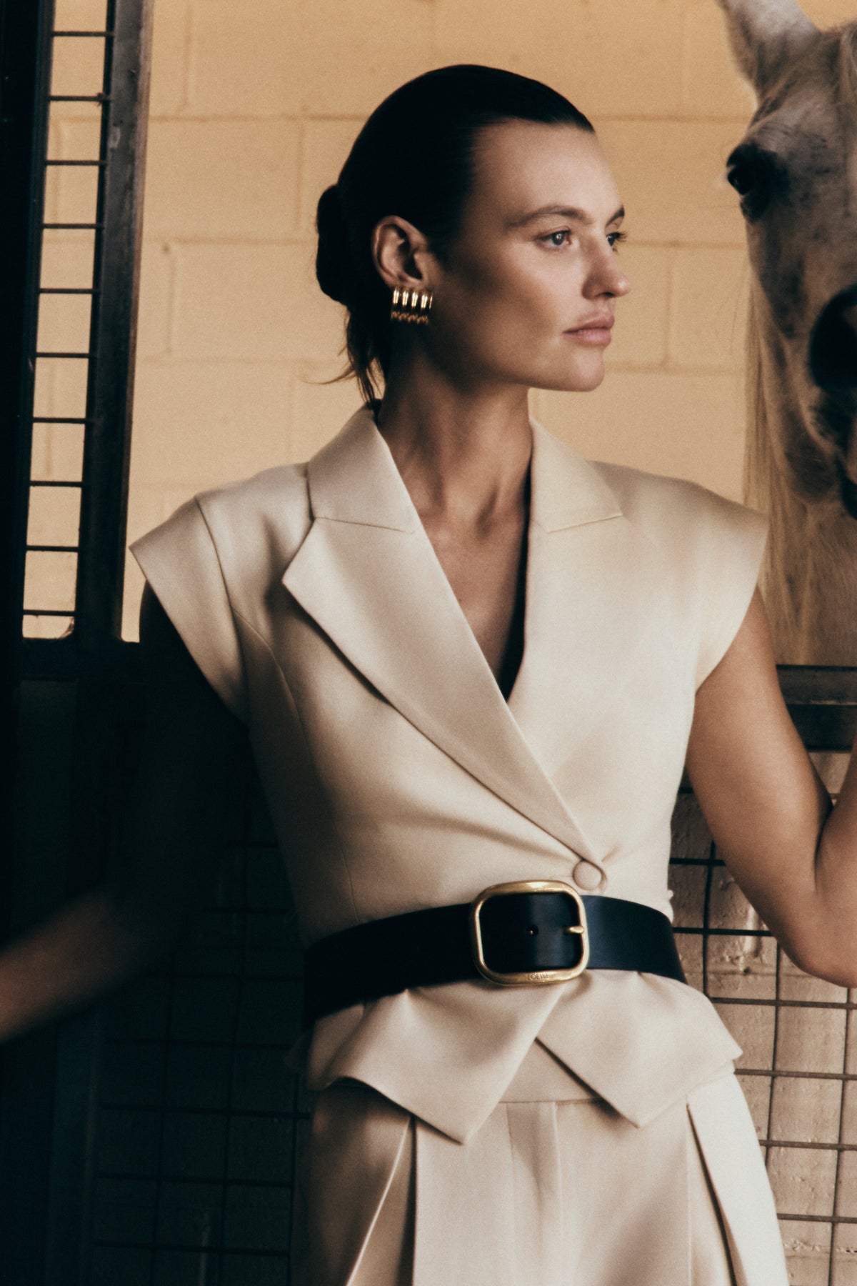 A model wearing a beige short-sleeve linen top with an asymmetric lapel neckline and a button closure. The top is paired with a mid-rise wide-leg linen pant.