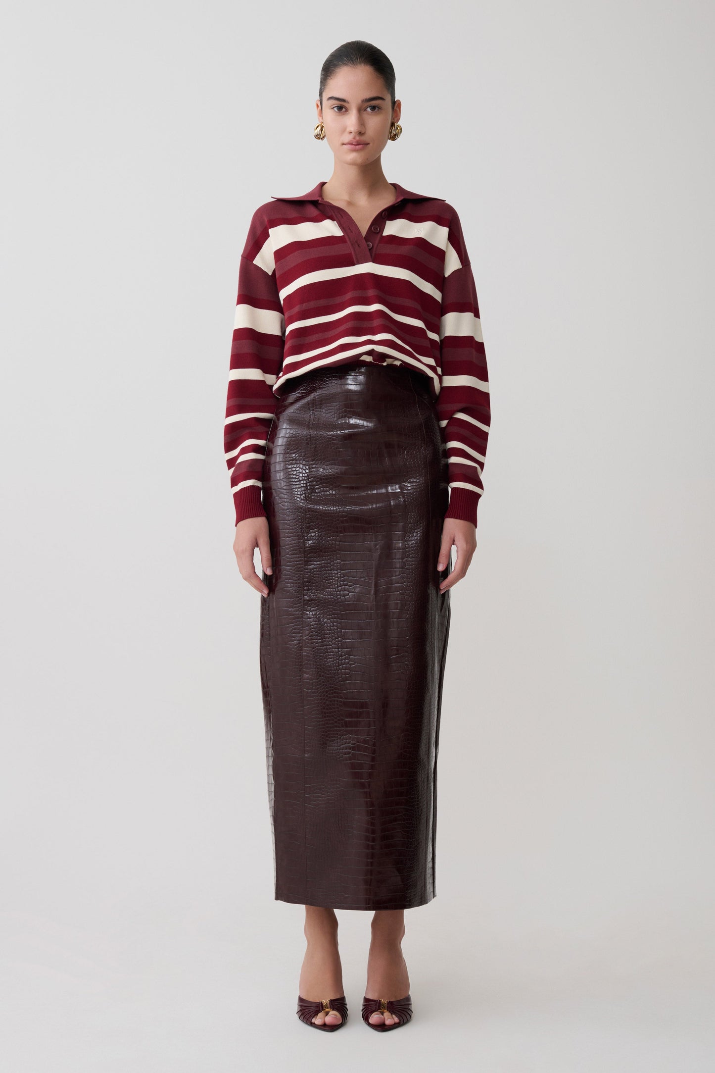 Woman wearing a striped sweater and leather skirt on a white background.