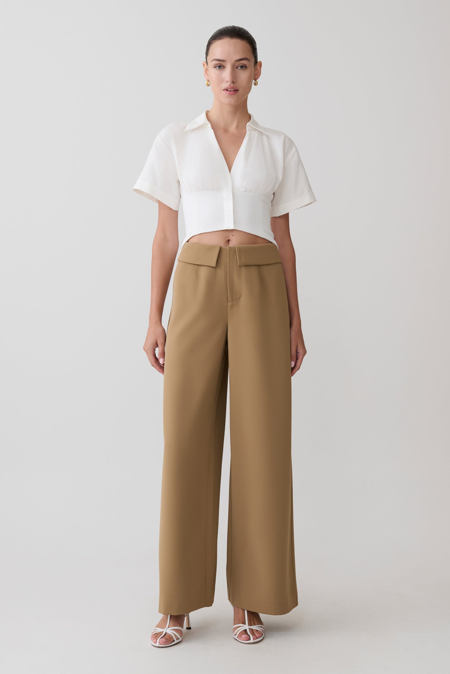 Woman wearing a white blouse and tan pants on a light gray background