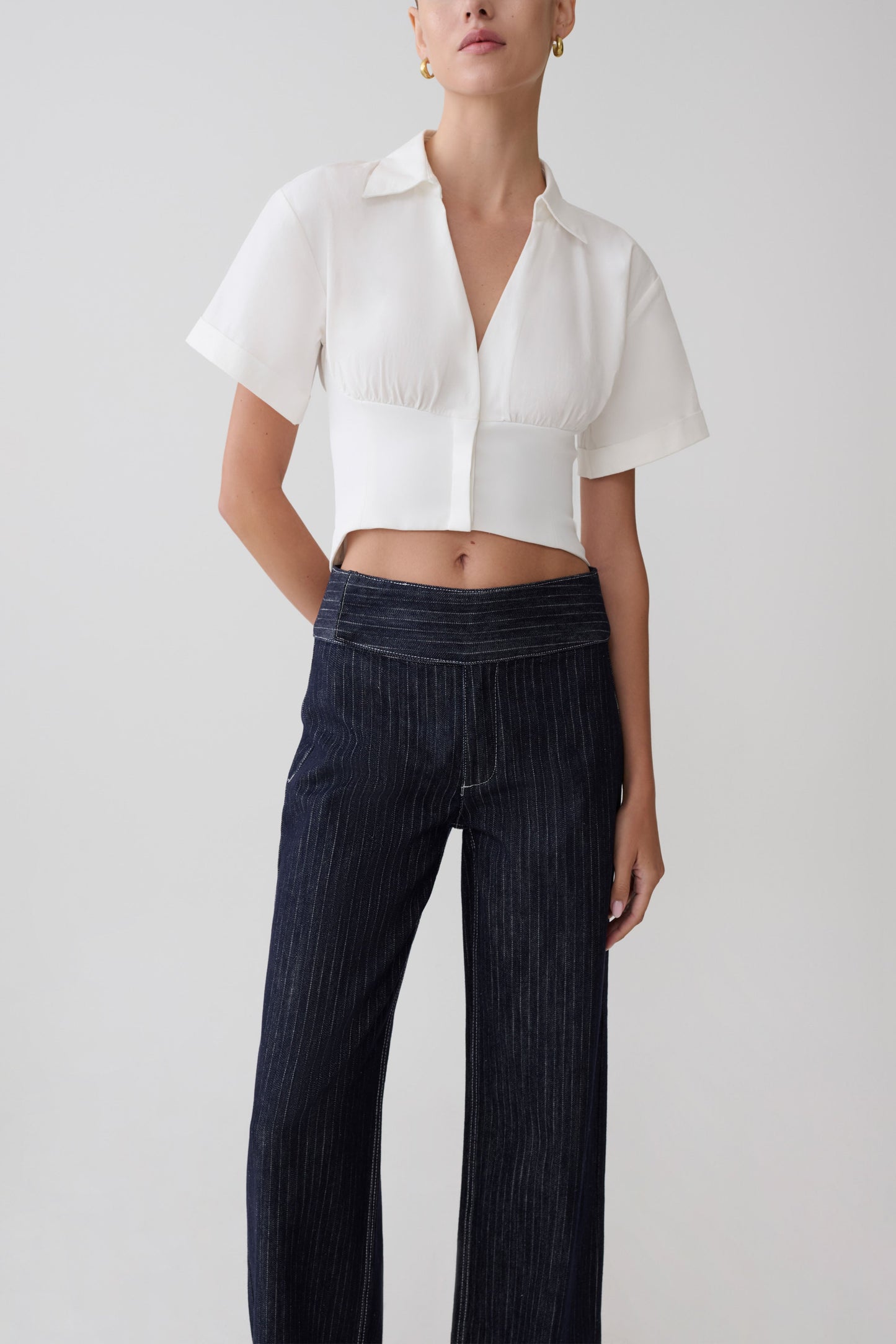 Woman wearing a white cropped shirt and dark striped denim jeans.