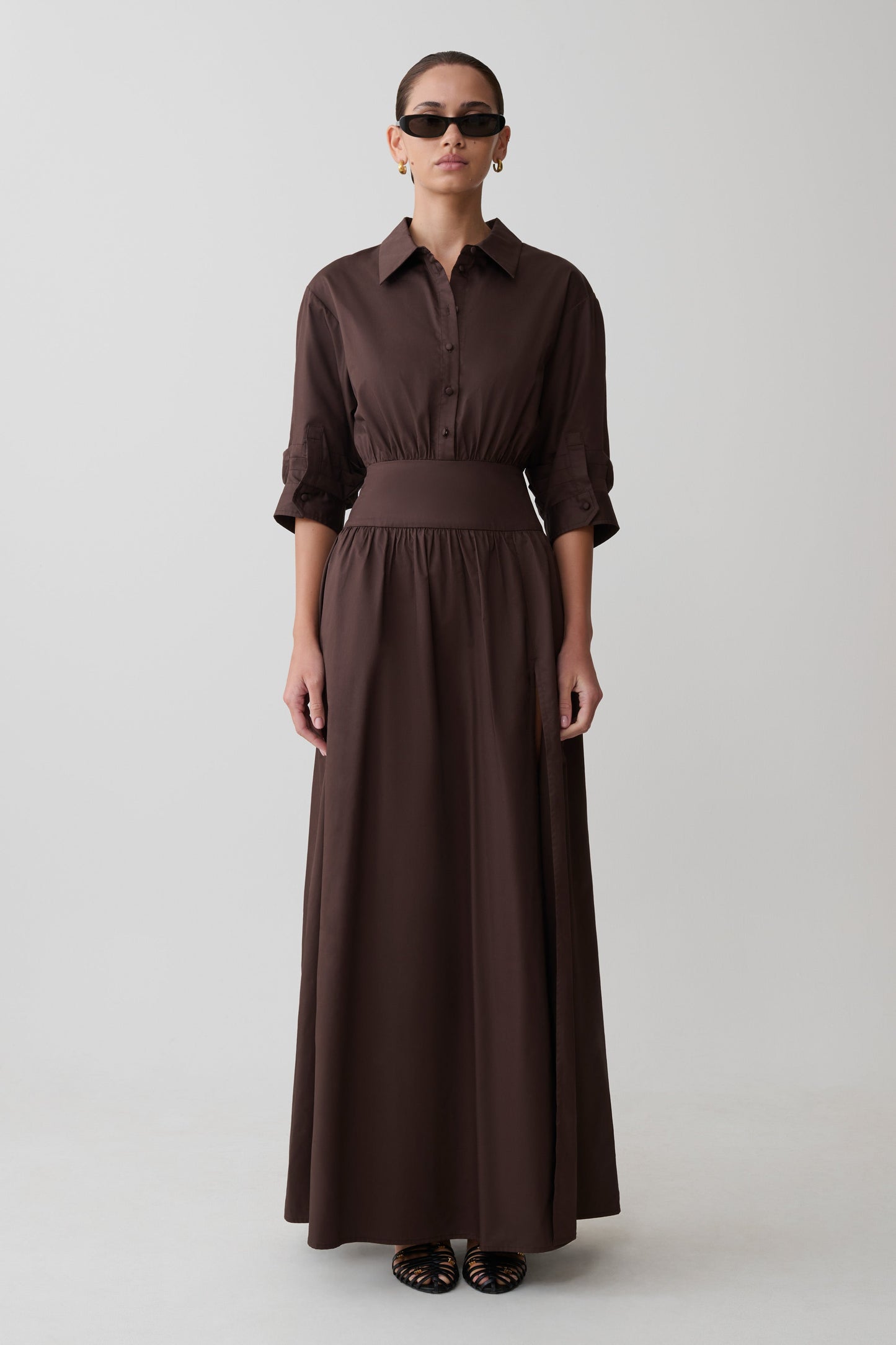 Woman wearing a long brown dress with a belt on a white background