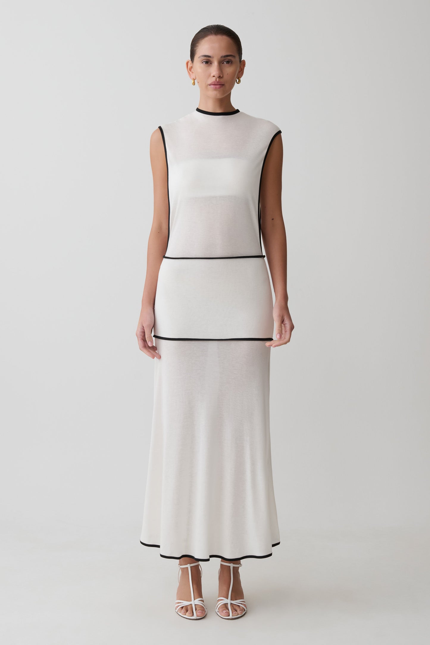 Woman wearing a sleeveless white dress with a black trim on a white background