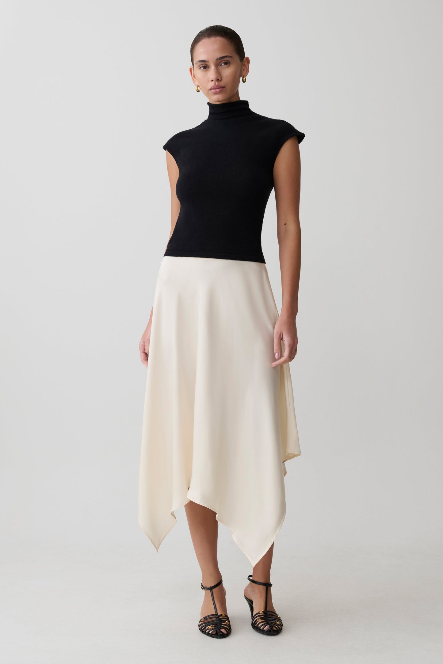 Woman wearing a black sleeveless top and white asymmetrical skirt.