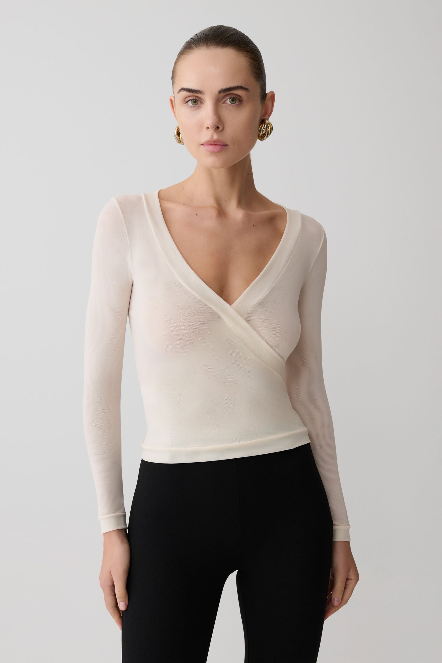 Woman wearing a cream long-sleeve top with a V-neckline on a plain background