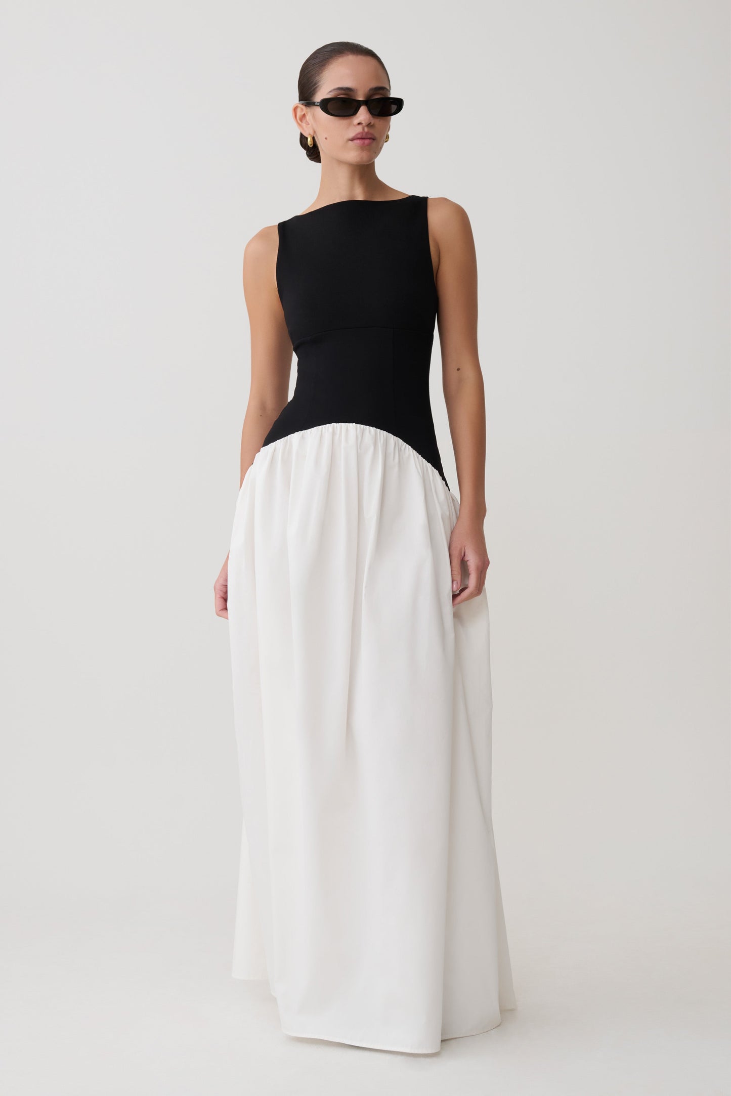 Woman wearing a black top and white pants on a plain background