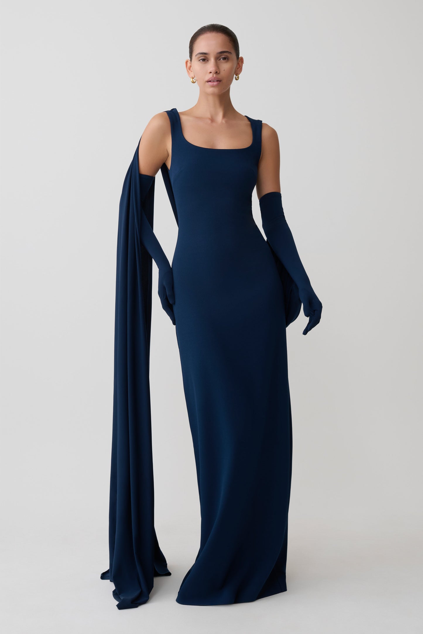 Woman wearing a long navy blue dress with a cape on a white background