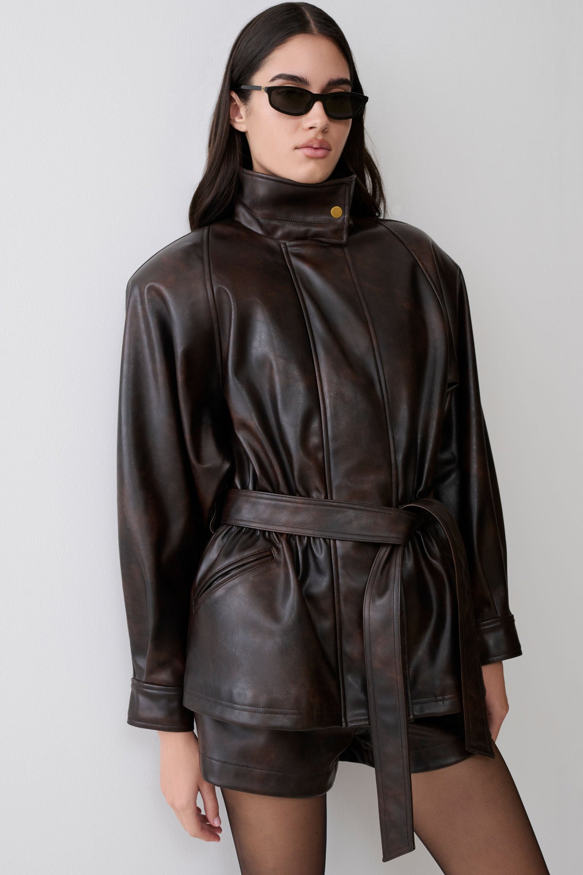 Woman wearing a dark brown faux leather cinch waist jacket.