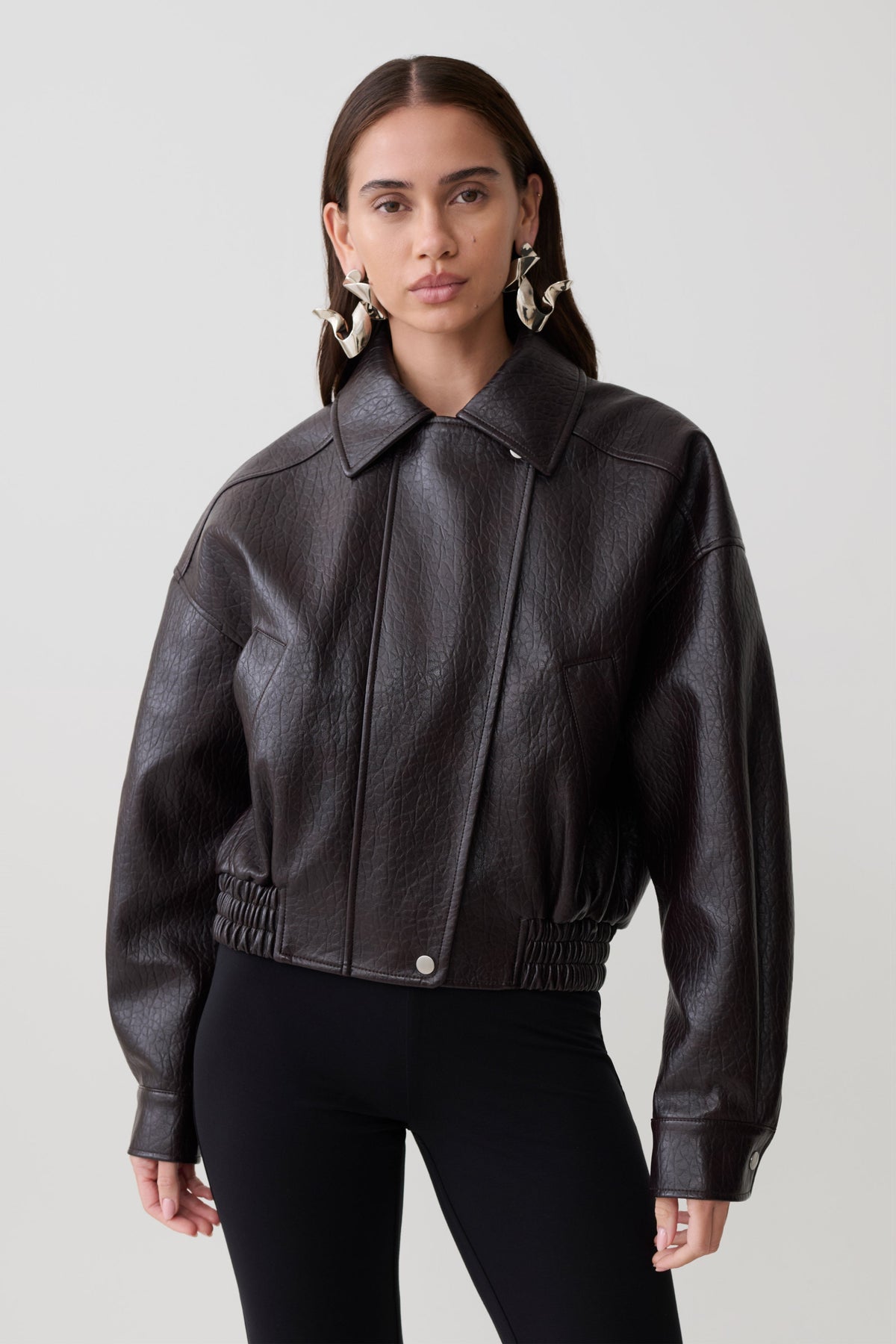 Woman wearing a brown faux leather cropped jacket.