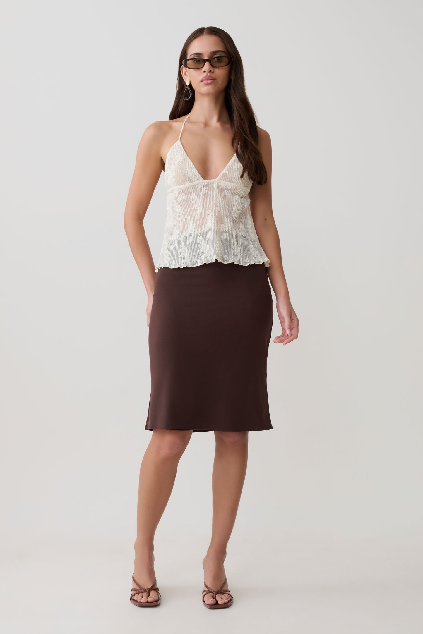 Woman wearing a white lace top and brown skirt.