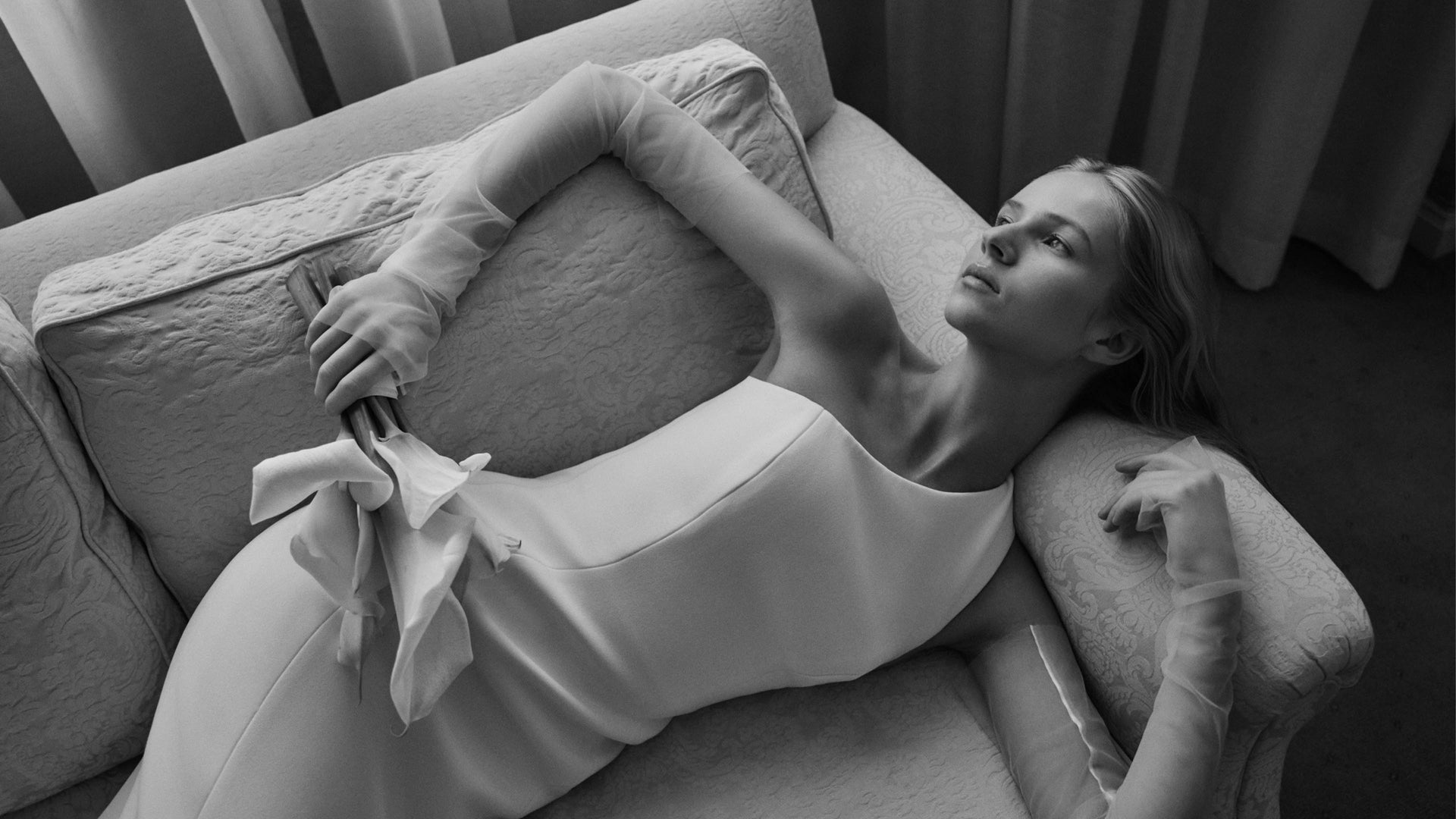 Woman lying on a couch with a white gown.