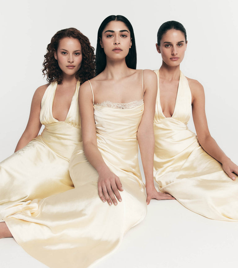 Three women in light yellow dresses sitting side by side against a white background.