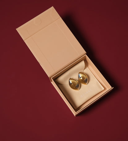 Gold earrings in a beige jewelry box on a red background.