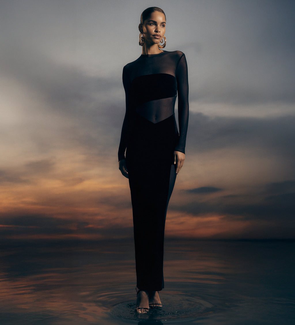 Woman in a black dress standing in water with a dramatic sky.