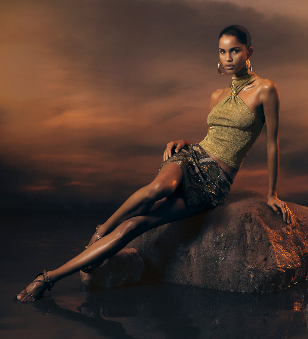 Woman in a green top and patterned skirt sitting on a rock with a dramatic sky.