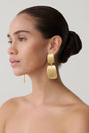 Woman wearing gold textured statement drop earrings.