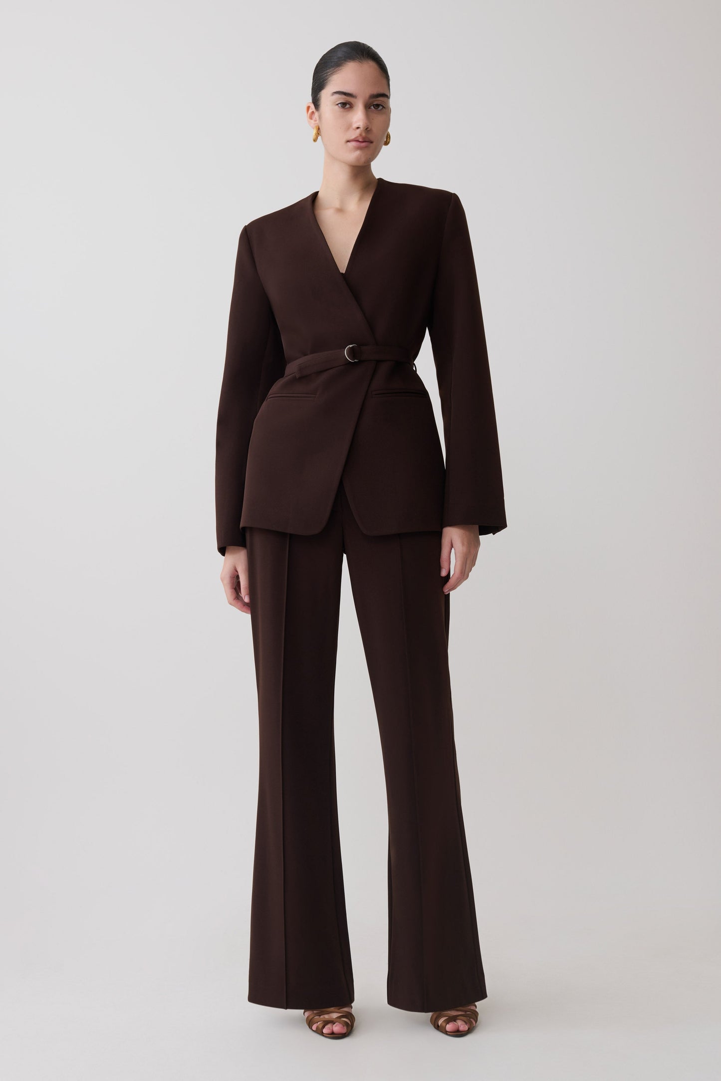 Woman wearing a dark brown drop shoulder suiting blazer with matching flare suiting pants.