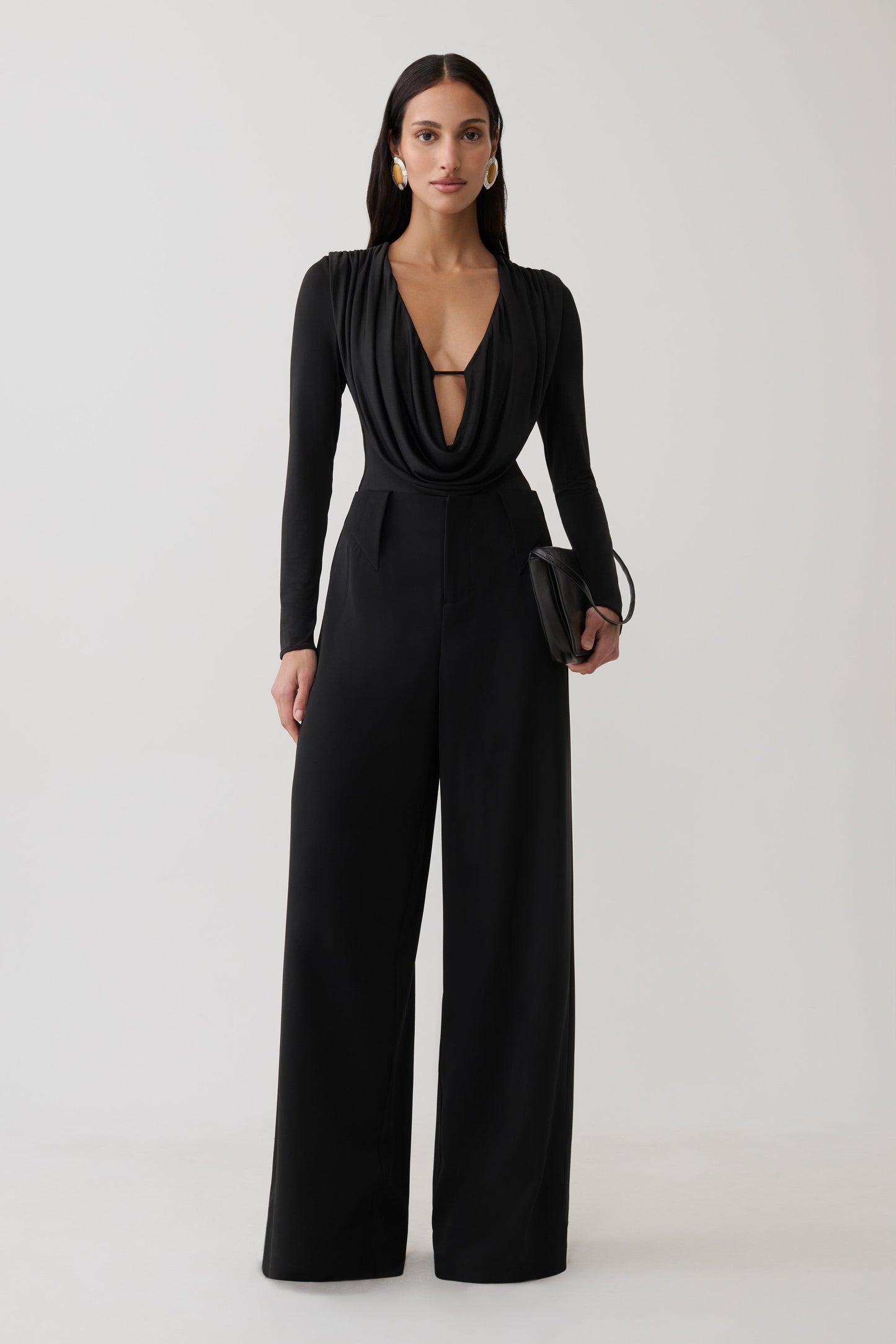 Woman wearing black cowl long sleeve slinky bodysuit, with black pants.