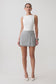 Woman wearing a white sleeveless top and grey wrap mini skirt.