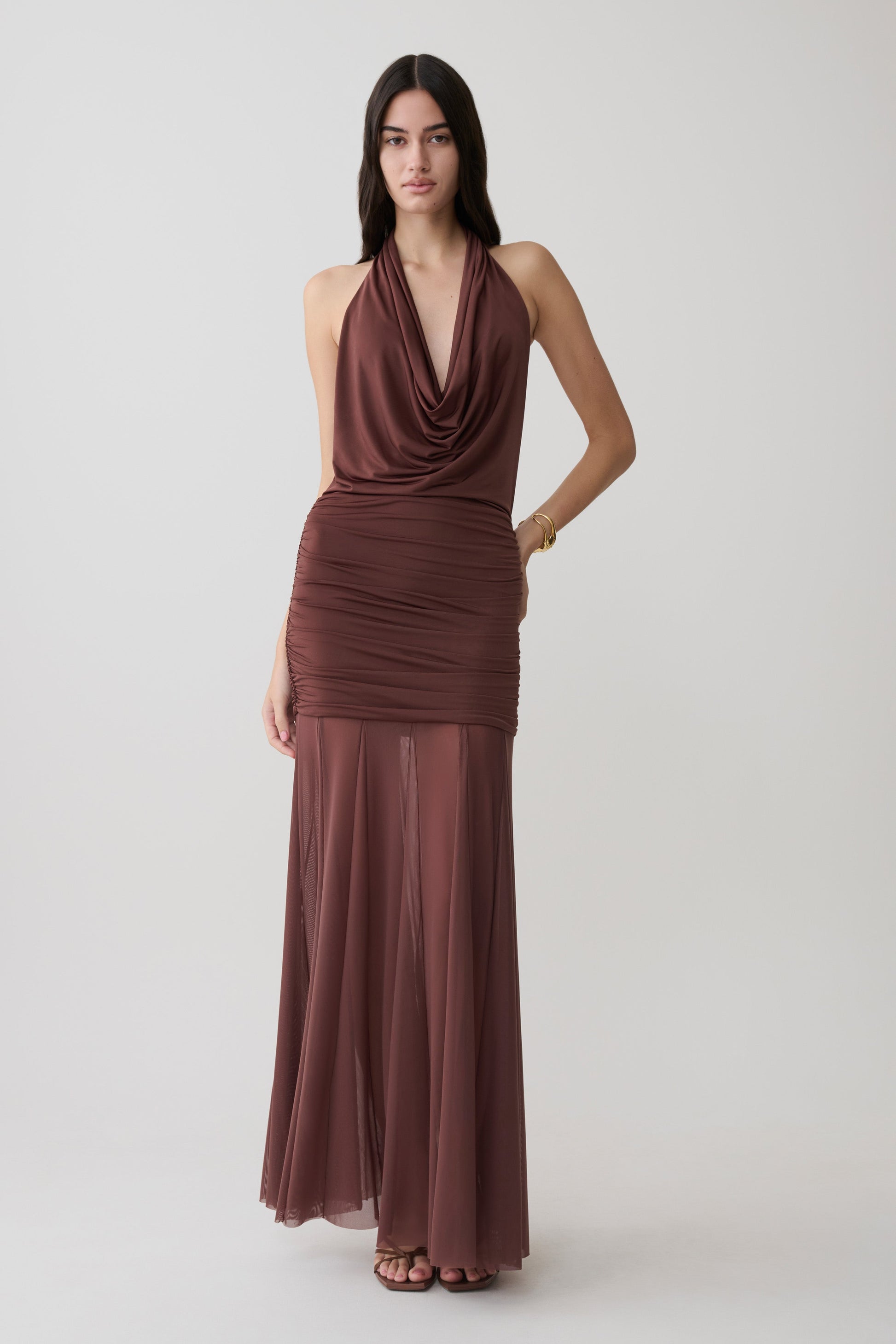 Woman wearing a brown draped halter slinky maxi dress.