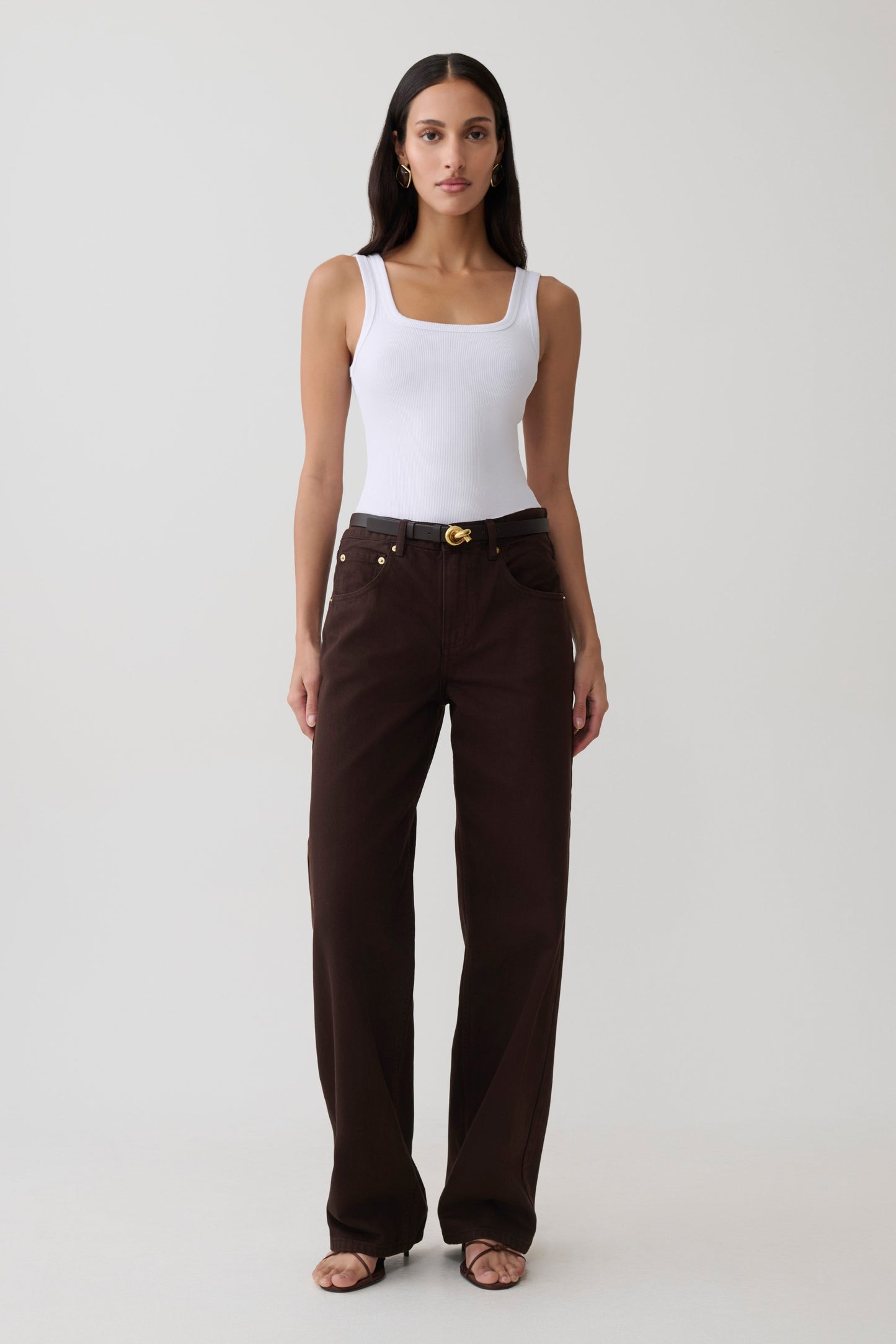 Woman wearing a white tank and brown mid rise denim jeans.