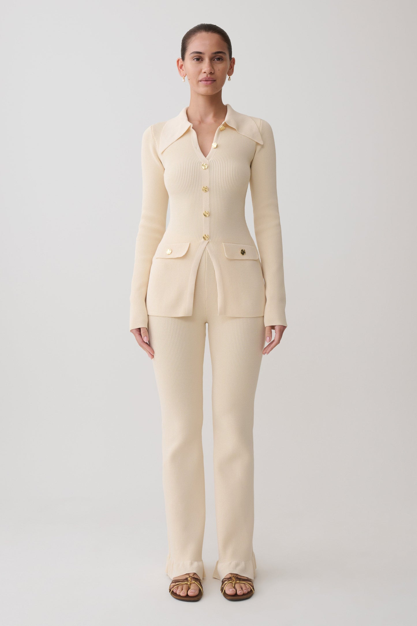 Woman wearing a white ribbed long sleeve longline top with ribbed flared pants.