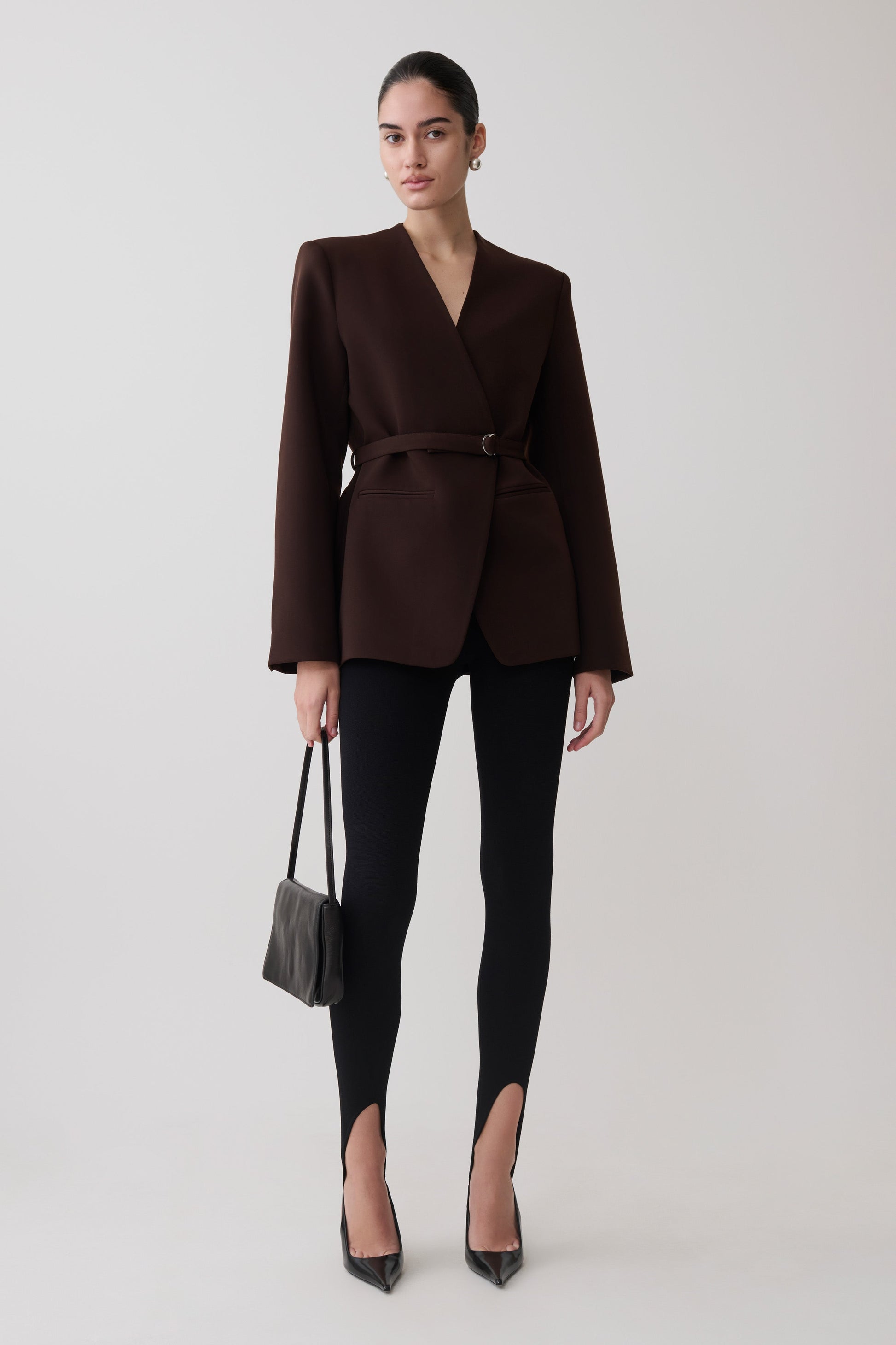 Woman wearing a brown blazer and knit black leggings.