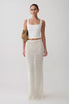 Woman wearing a white sleeveless top and white knit crochet skirt.