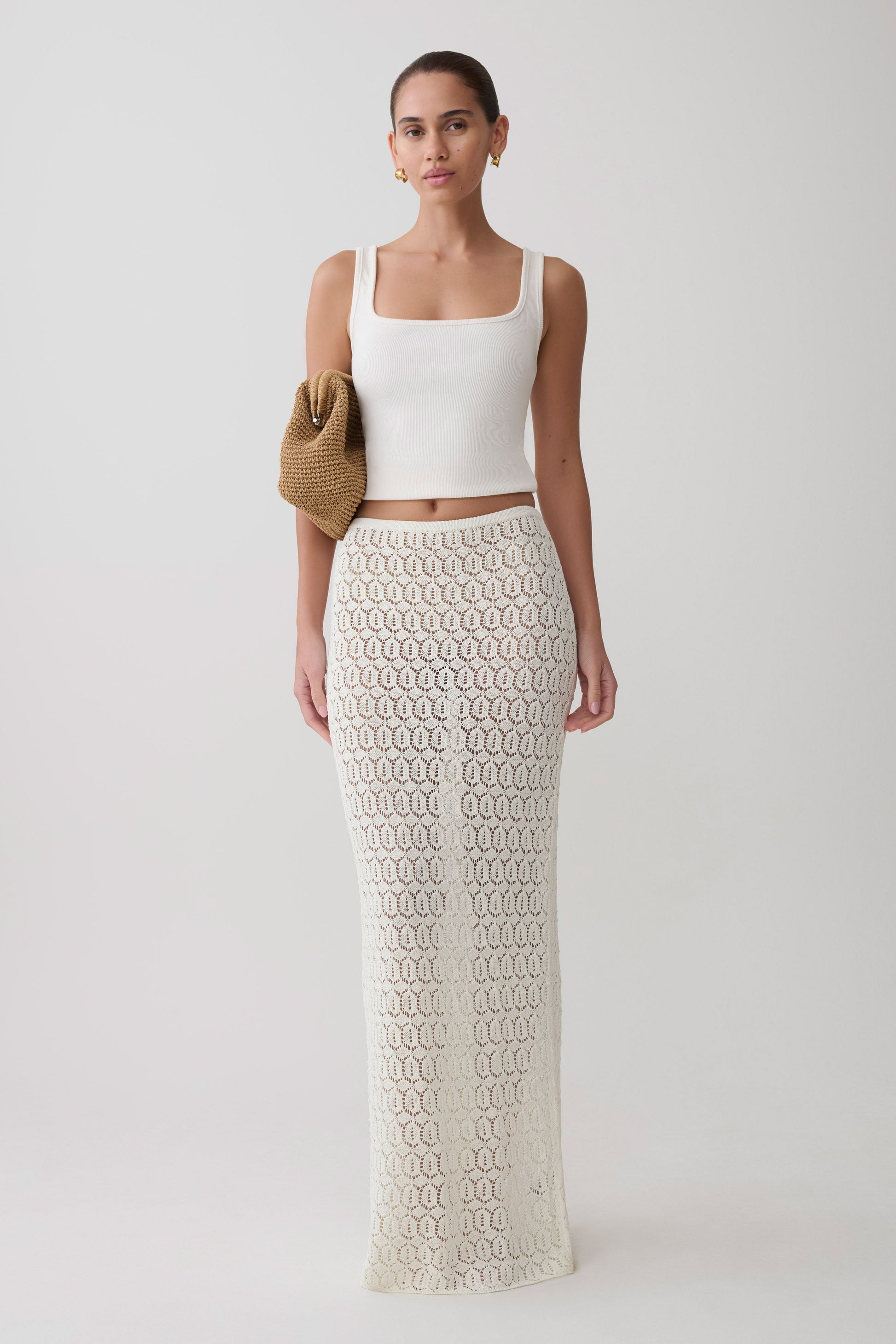 Woman wearing a white sleeveless top and white knit crochet skirt.