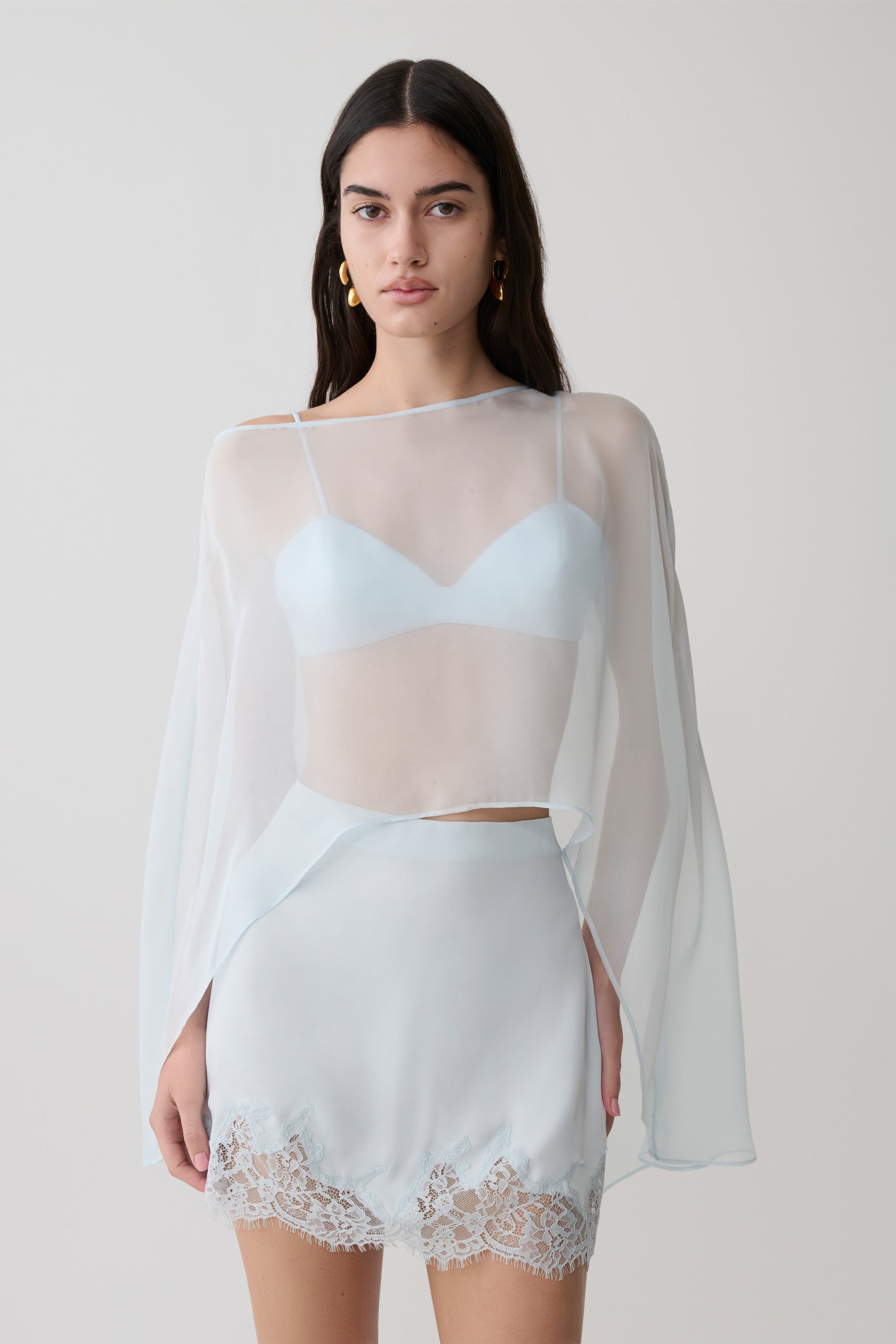 Woman wearing light blue bralette with chiffon cape with matching lace and satin mini skirt.