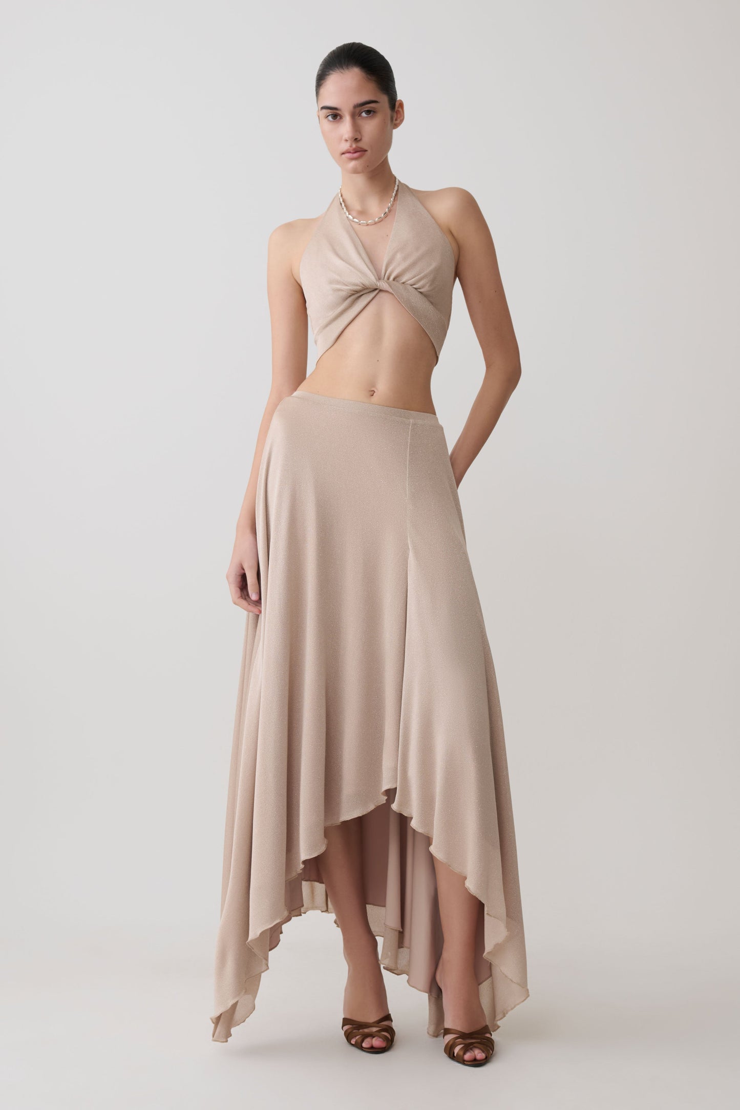 Woman wearing a gold draped lurex halter top with matching maxi skirt.