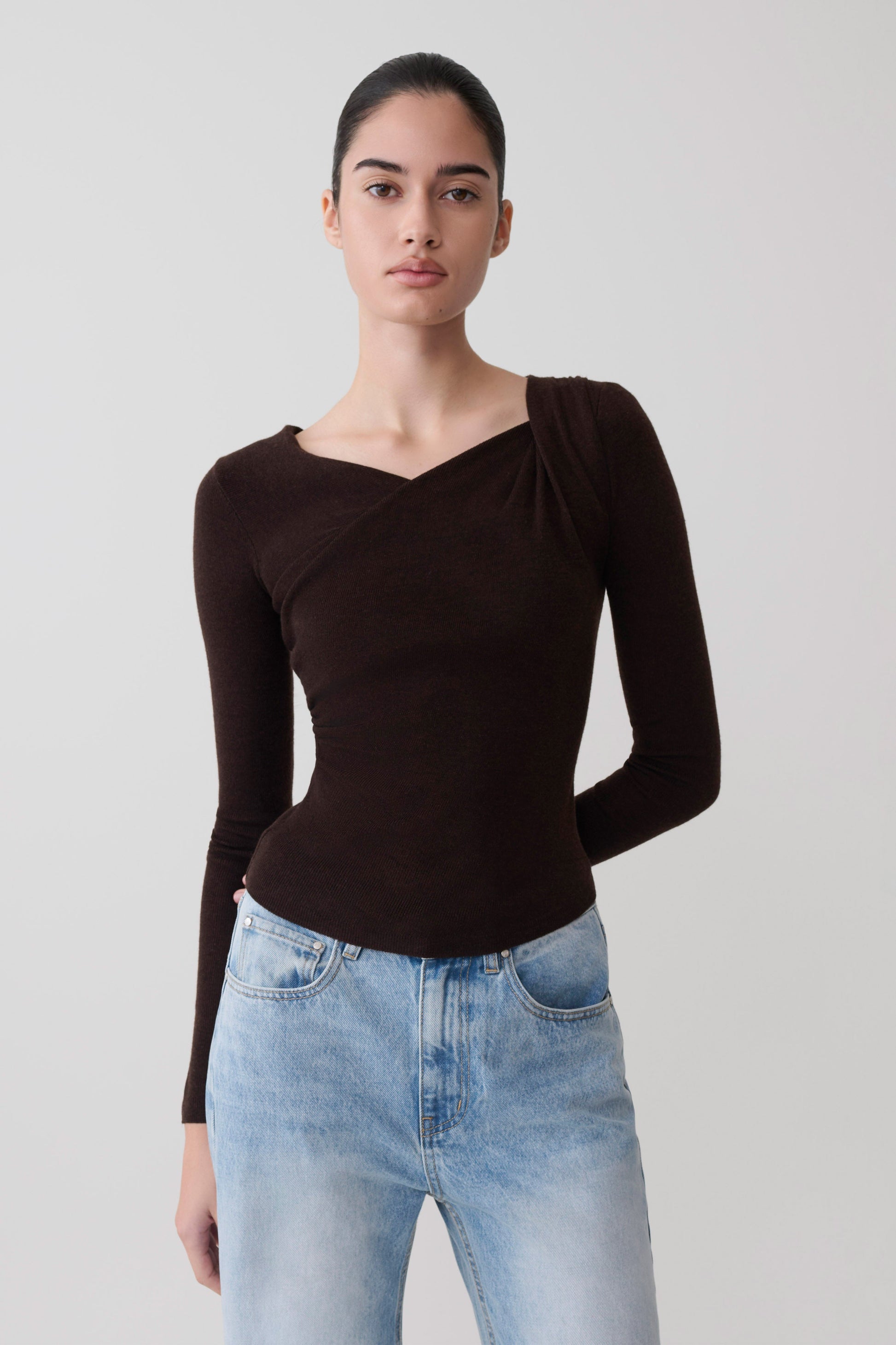 Woman wearing a brown long-sleeve draped twist knit top.