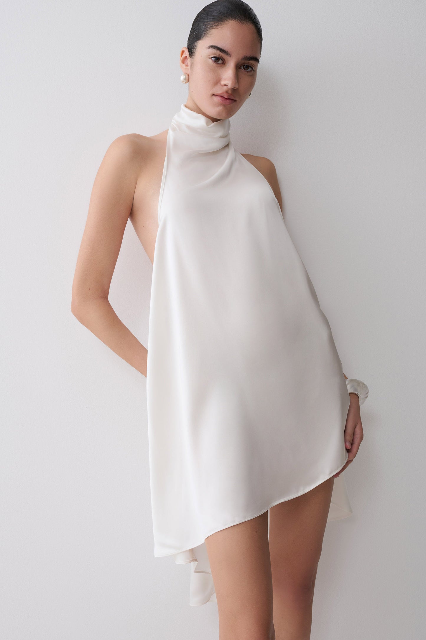 Woman wearing a white asymmetrical satin halter mini dress.