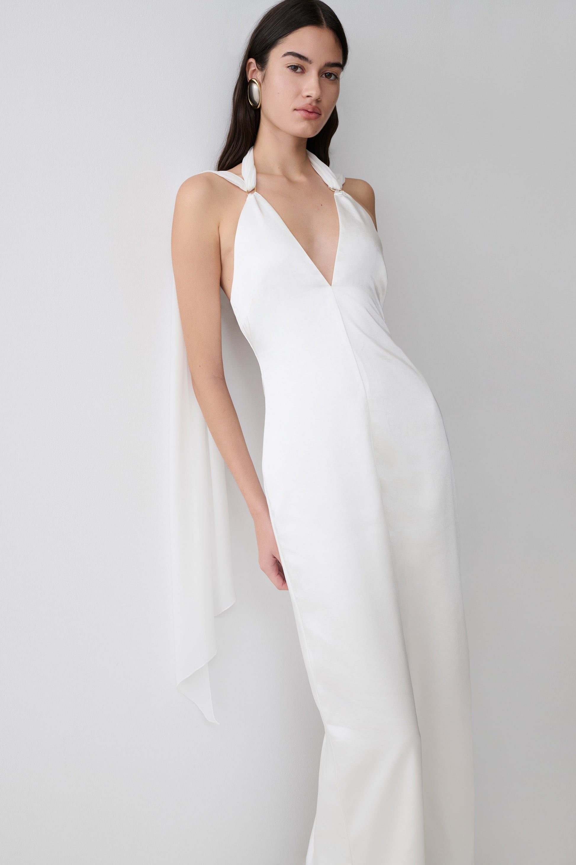 Woman wearing a white satin maxi dress with draped shoulders.