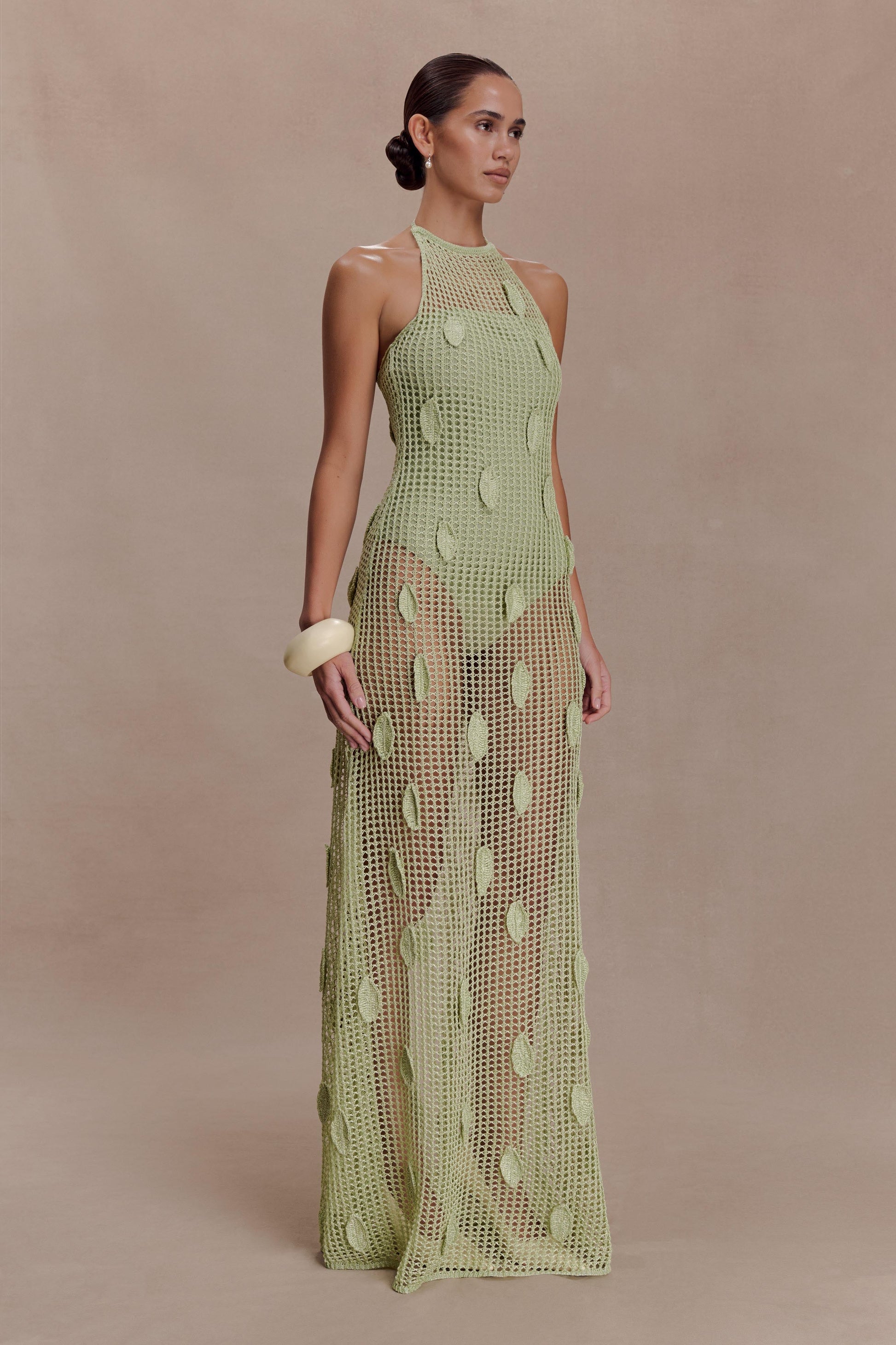 Woman wearing a sheer green crochet halter maxi dress with intricate leaf detailing.
