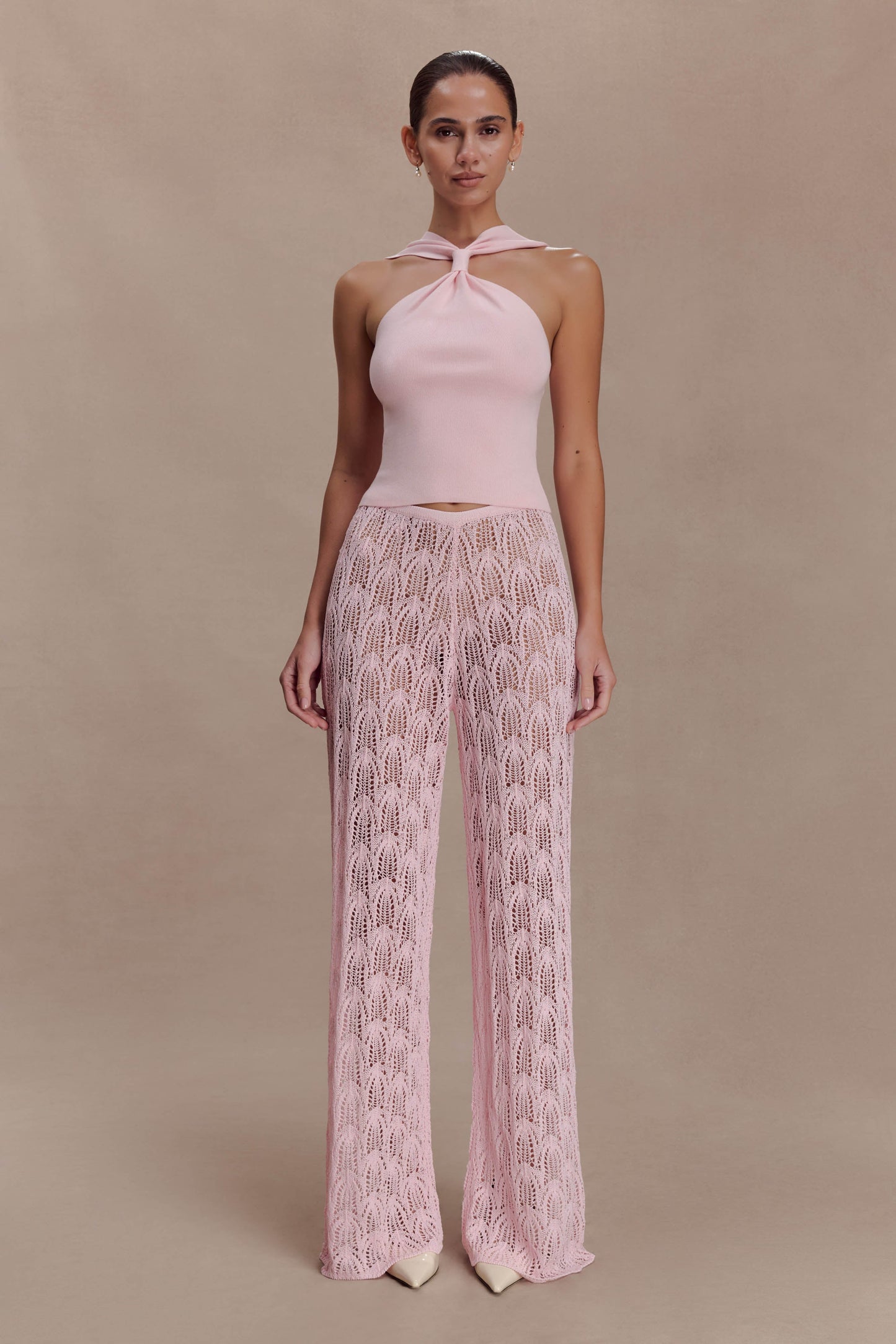 Woman wearing a pink knit top and crochet pants.