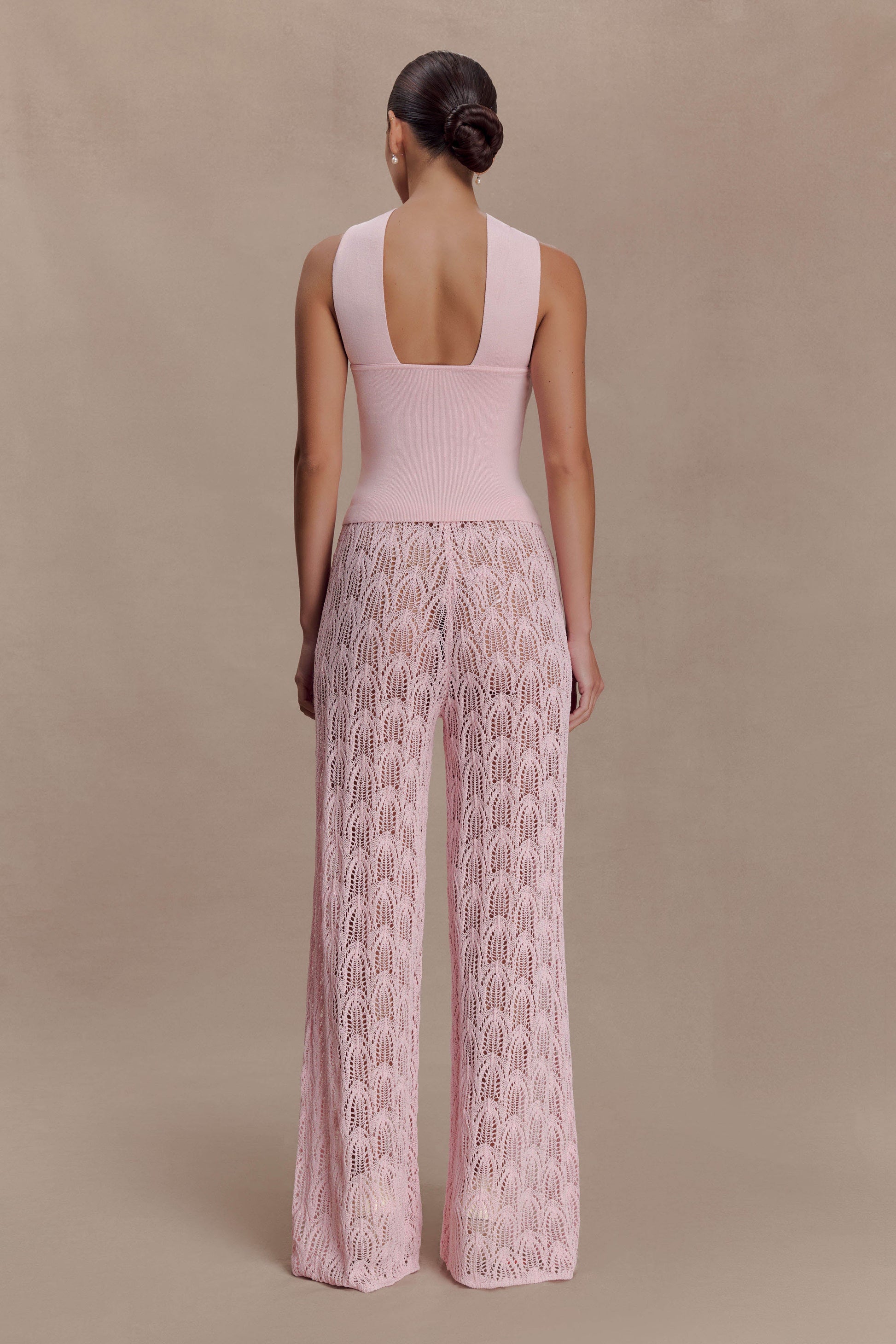 Woman wearing a pink knit top and crochet pants.