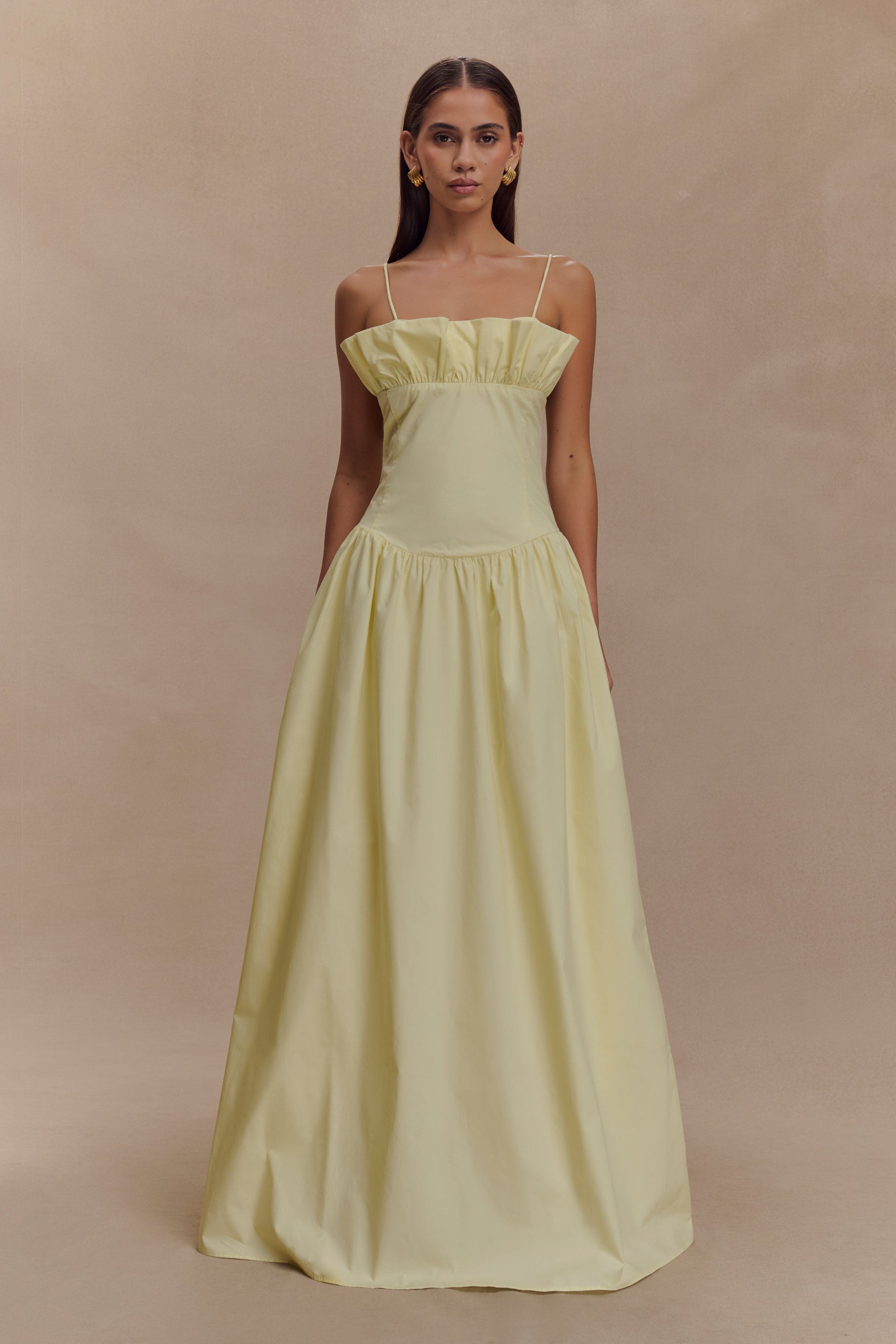 A model wearing a lemon yellow maxi dress with a frill-gathered neckline and slender spaghetti straps.