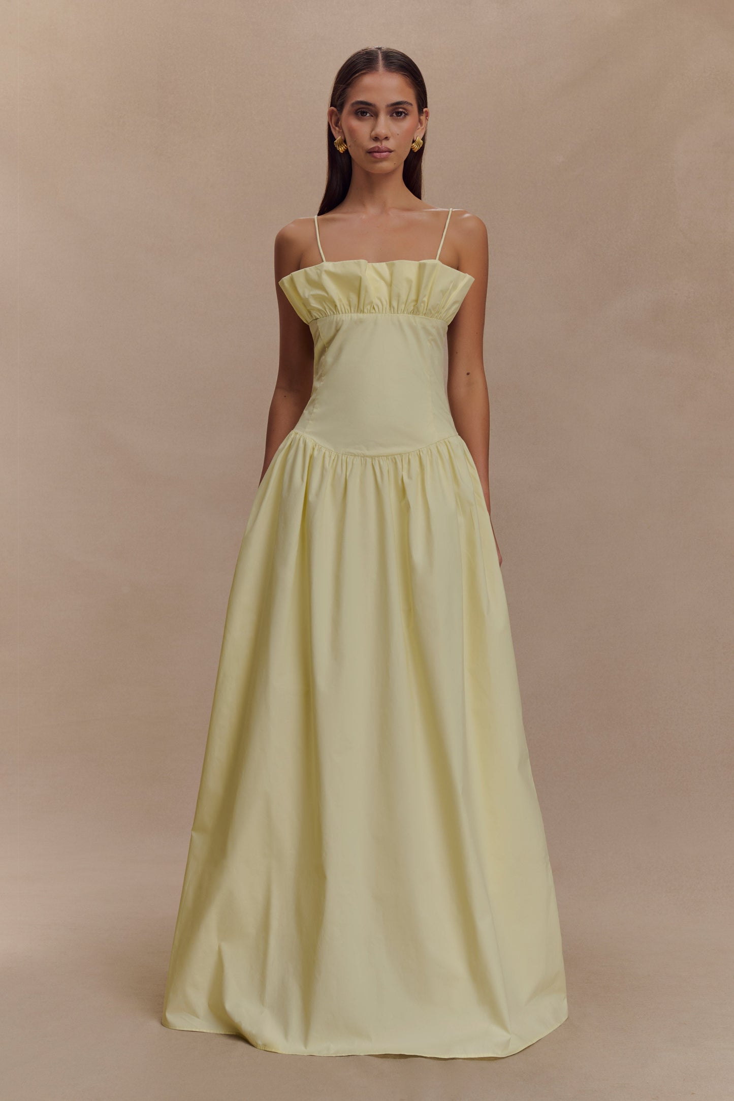 A model wearing a lemon yellow maxi dress with a frill-gathered neckline and slender spaghetti straps.