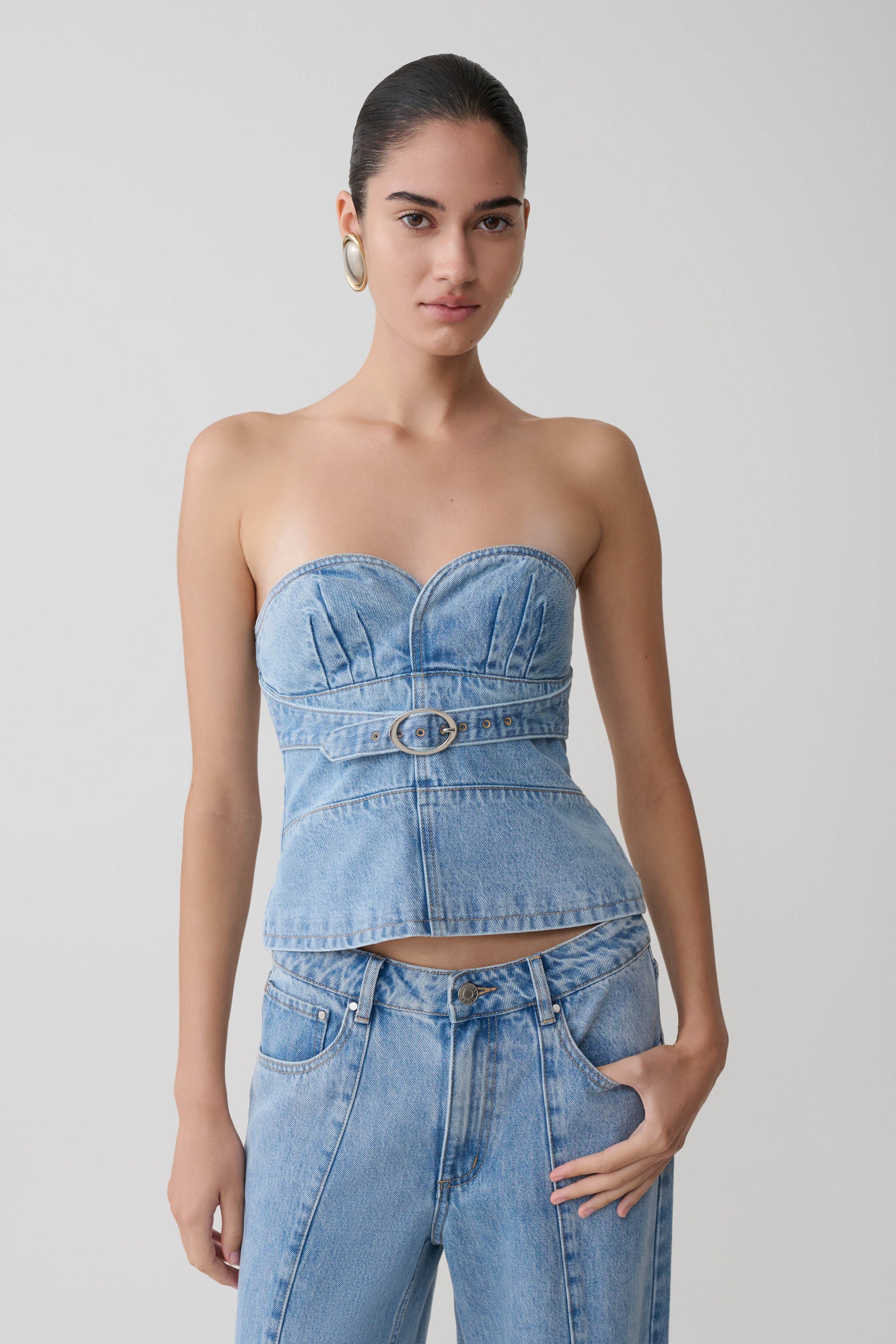 Woman wearing a denim strapless top and high-waisted jeans against a plain background.