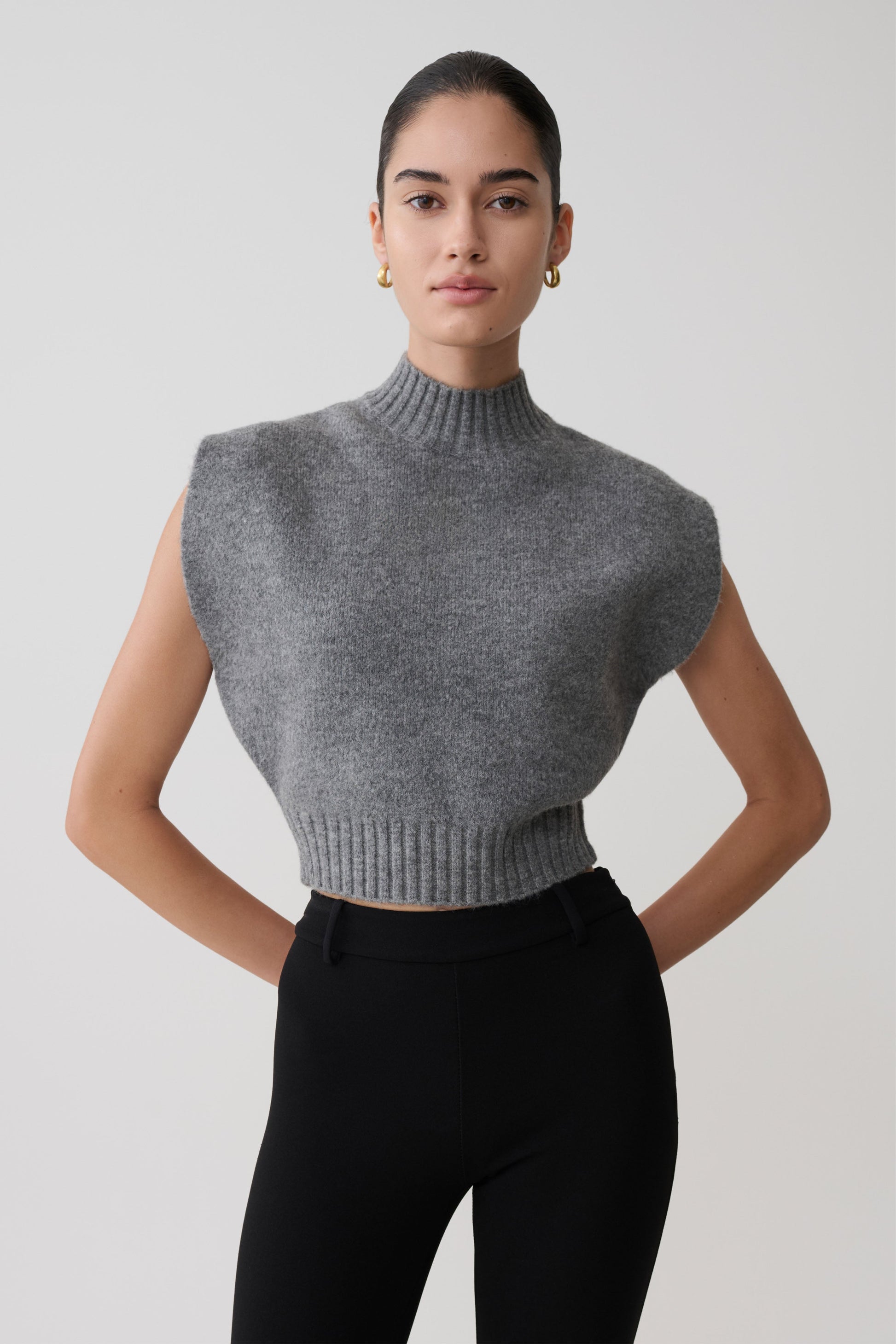 Woman wearing a gray sleeveless knit top against a plain background.