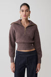 Woman wearing a brown cropped sweater with a high collar and zipper on a plain background.
