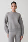 Woman wearing a gray sweater and pants on a plain background.