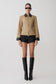 Person wearing a beige jacket with black accents, black shorts, and black knee-high boots on a white background.