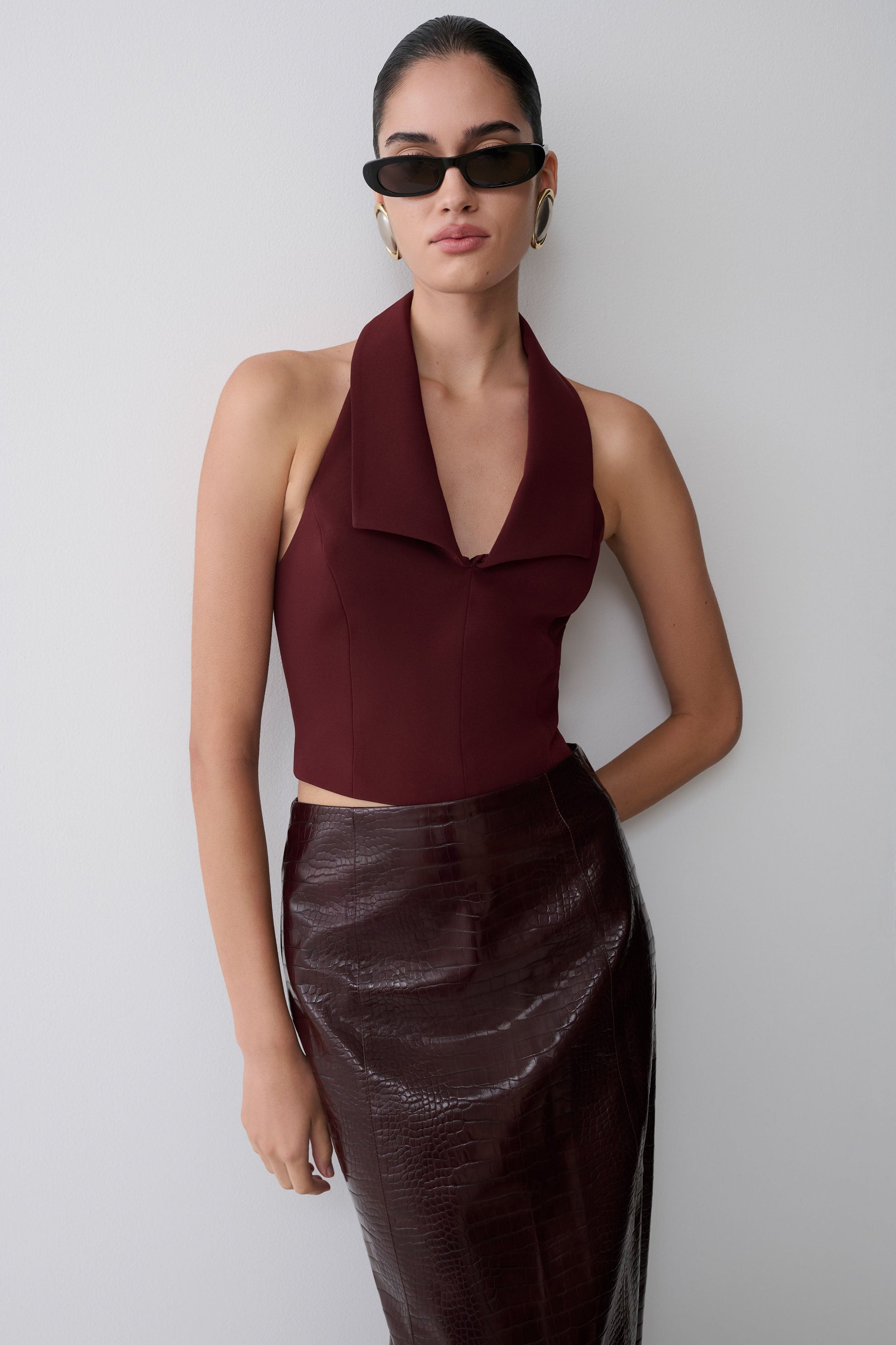 Woman wearing a burgundy halter top and black skirt against a plain background.